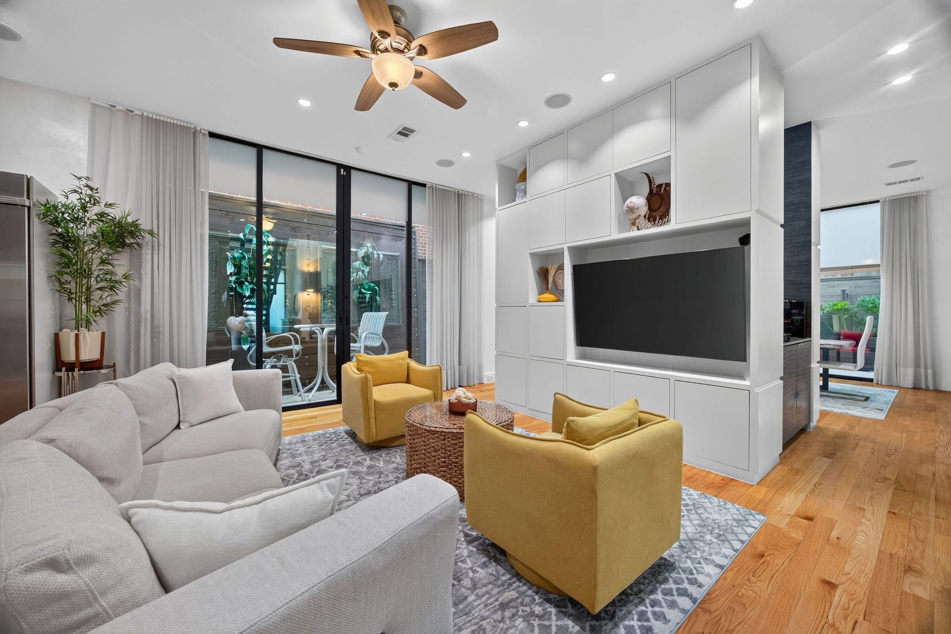 1310 Nantucket Drive, Houston, TX 77057 Bright and modern living space featuring a sleek built-in entertainment center, cozy seating, and expansive sliding glass doors leading to an inviting outdoor patio.