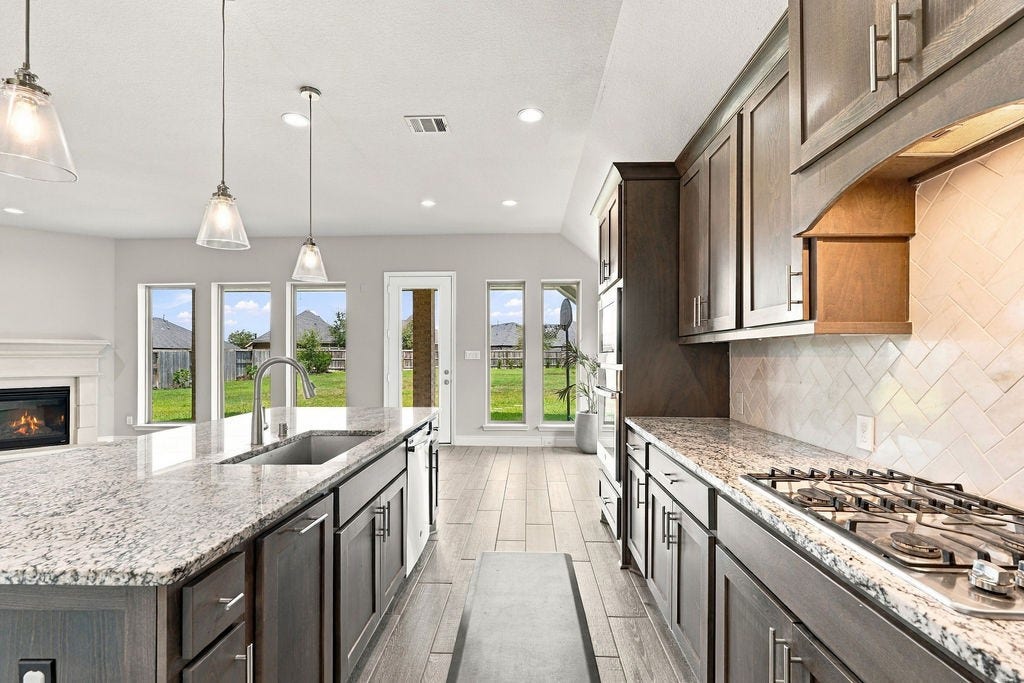 6914 Red Oak Drive, Katy, TX 77493 Stunning modern kitchen with granite countertops, elegant pendant lighting, and a seamless open layout that leads to a bright, inviting backyard view.