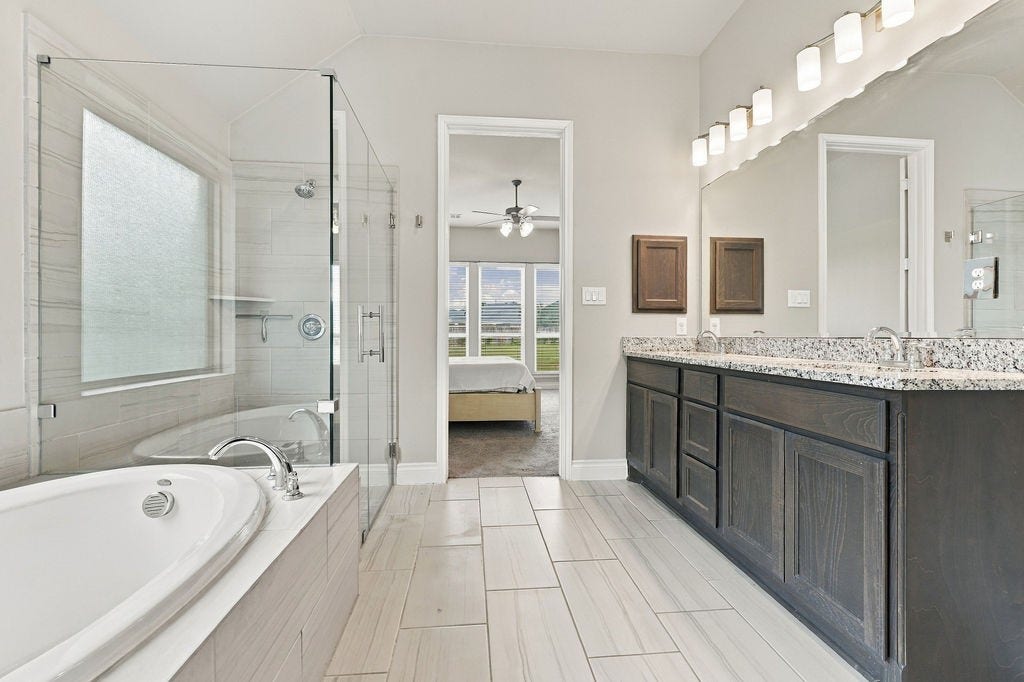 6914 Red Oak Drive, Katy, TX 77493 Luxurious bathroom featuring a spacious glass-enclosed shower, elegant double vanity, and inviting soaking tub, with a glimpse into a bright bedroom.