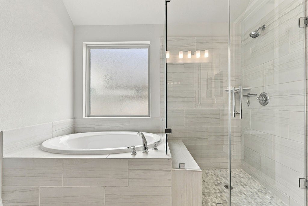 6914 Red Oak Drive, Katy, TX 77493 Luxurious bathroom featuring a spacious glass-enclosed shower and a relaxing soaking tub, complemented by elegant tilework and a frosted window for privacy.