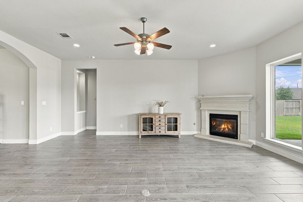 6914 Red Oak Drive, Katy, TX 77493 Spacious living room featuring elegant wood-look tile flooring, a cozy fireplace, and large windows that flood the space with natural light.