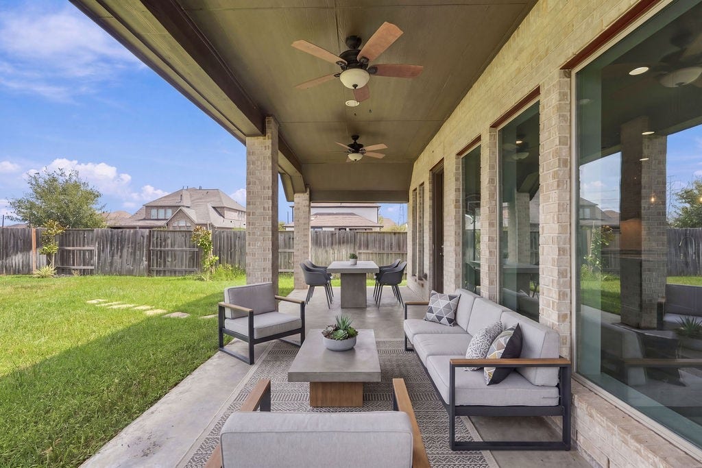 6914 Red Oak Drive, Katy, TX 77493 Expansive covered patio with stylish seating, ceiling fans, and a view of the spacious fenced backyard, perfect for outdoor entertaining.