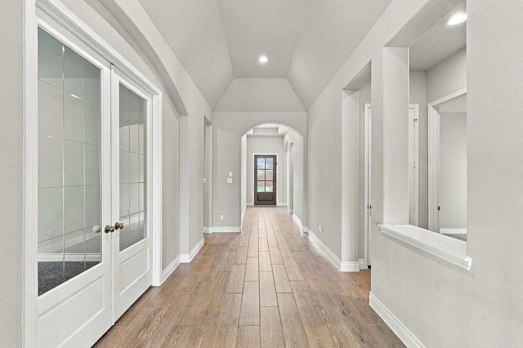 6914 Red Oak Drive, Katy, TX 77493 Elegant hallway with arched ceilings, hardwood floors, and stylish French doors, leading to a bright entrance.
