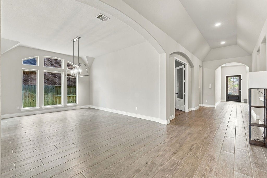 6914 Red Oak Drive, Katy, TX 77493 Spacious open-concept living area with high ceilings, elegant arched entryways, and abundant natural light from large windows, featuring modern wood-look flooring and stylish lighting fixtures.
