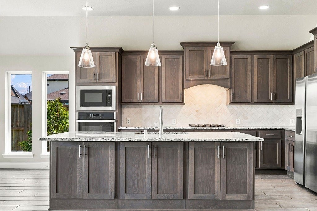 6914 Red Oak Drive, Katy, TX 77493 Elegant kitchen featuring dark wood cabinetry, a spacious island with granite countertops, and modern stainless steel appliances, all complemented by sleek pendant lighting.