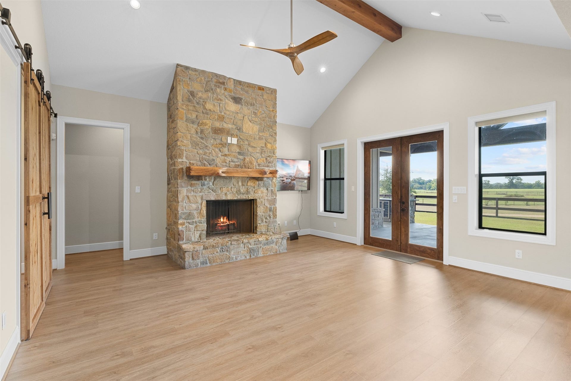 30163 High Spirit Ranch Road, Hempstead, TX 77445 Living room view shows the barn door entrance to the study, and hallway to the secondary bedrooms. Wooden double doors lead out to the patio and outdoor kitchen. Stone fireplace with custom wood mantle adds warmth and charm.