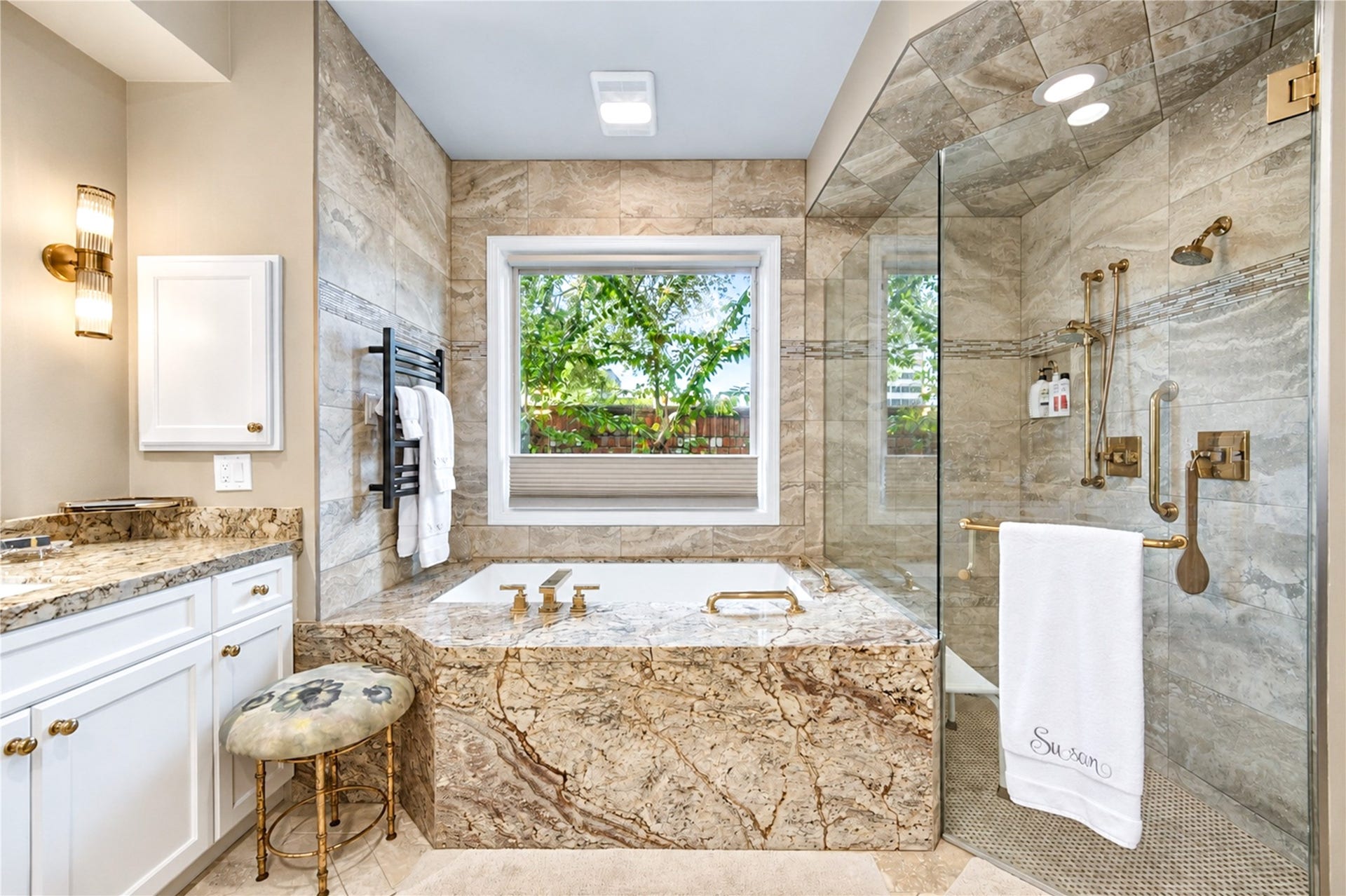 4 Milan Estates, Houston, TX 77056 The first-floor primary bath showcases a granite-clad air-jet tub, a frameless glass shower, a towel warmer and a window overlooking greenery.