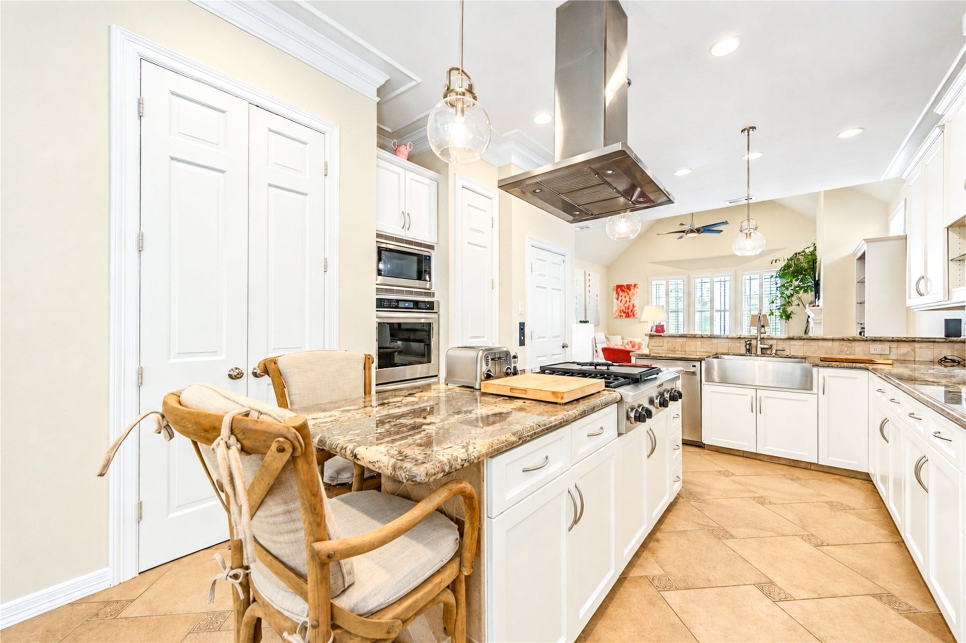4 Milan Estates, Houston, TX 77056 The island cooktop, stainless hood and white cabinetry open to a vaulted family area filled with light from a wall of windows.