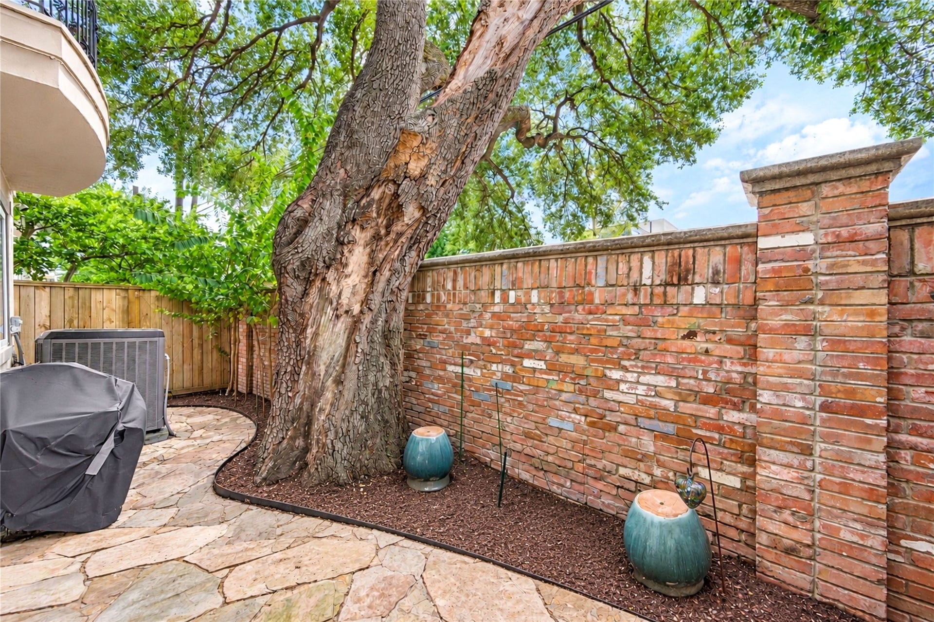 4 Milan Estates, Houston, TX 77056 A flagstone patio beneath a mature oak is enclosed by a brick wall, creating a private outdoor retreat.