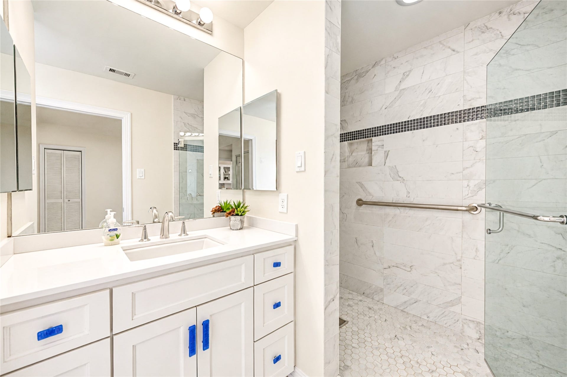4 Milan Estates, Houston, TX 77056 A bright vanity with a light countertop faces a frameless walk-in shower finished with a mosaic accent band.