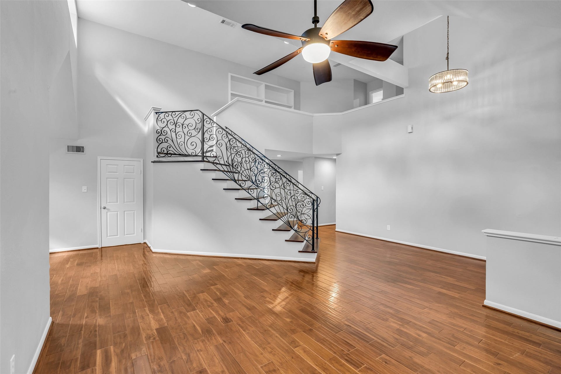 54 Sky Terrace Place, The Woodlands, TX 77381 Spacious living area featuring elegant hardwood floors and a stunning wrought-iron staircase, accentuated by a modern ceiling fan and ample natural light.