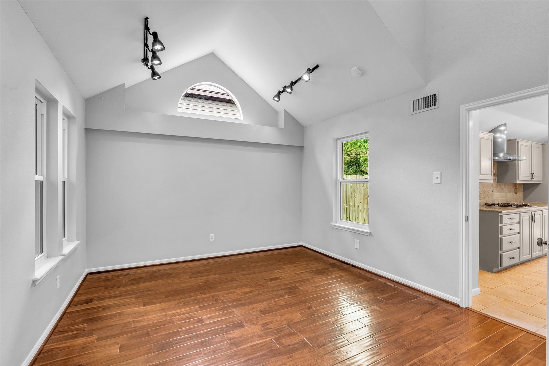 54 Sky Terrace Place, The Woodlands, TX 77381 Versatile and bright space ideal for a formal living room, home office, or flex room, featuring vaulted ceilings, a charming arched window, elegant hardwood floors, and modern track lighting, conveniently located adjacent to the spacious kitchen.
