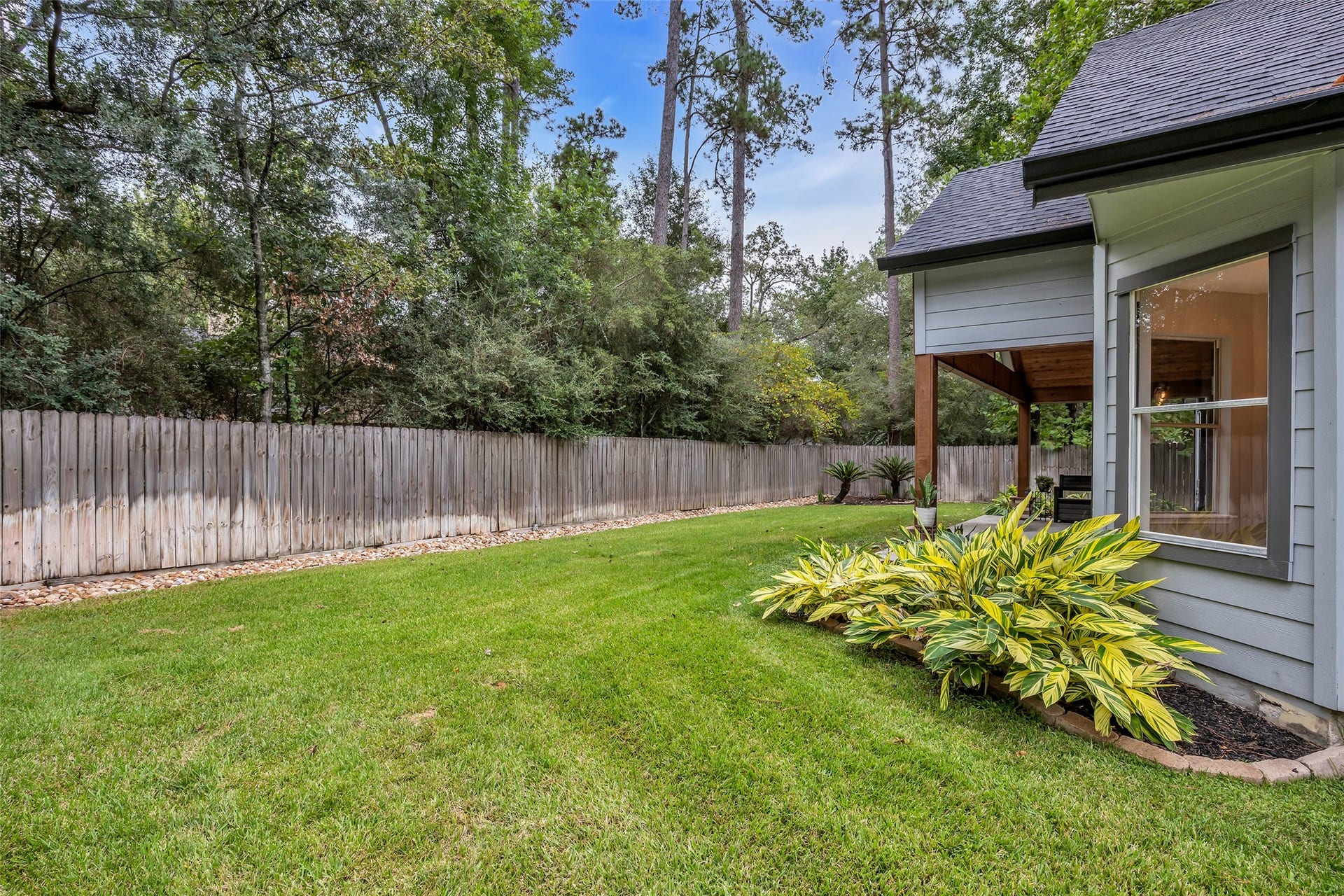 54 Sky Terrace Place, The Woodlands, TX 77381 Charming backyard with lush green lawn, mature trees, and a cozy covered patio perfect for relaxation.