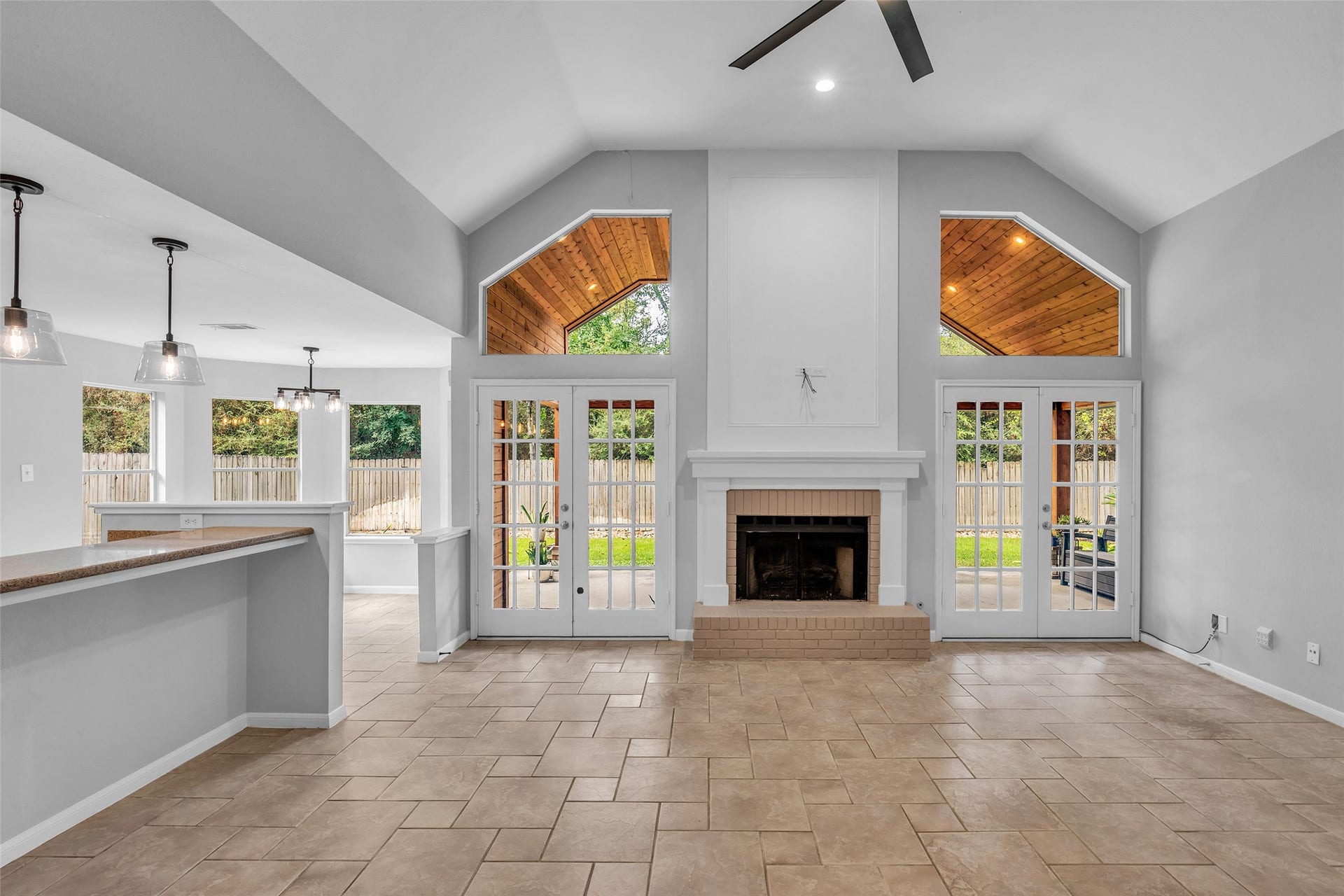 54 Sky Terrace Place, The Woodlands, TX 77381 Another view of the spacious living area featuring soaring vaulted ceilings, a cozy fireplace, and elegant French doors that bring in abundant natural light and open to the covered patio, creating a seamless connection between indoor and outdoor living.