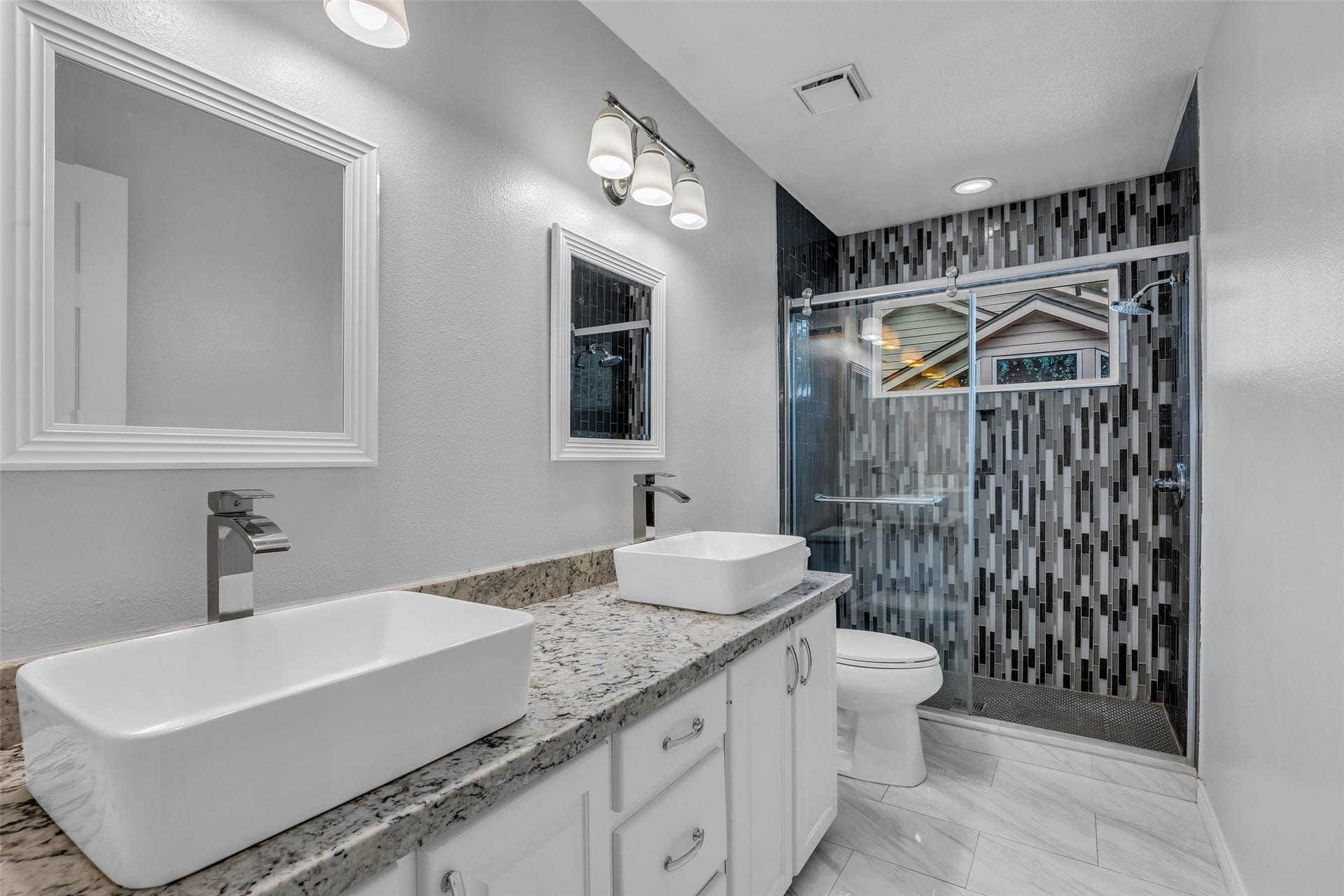 54 Sky Terrace Place, The Woodlands, TX 77381 Modern bathroom featuring a stylish dual-sink vanity with granite countertops and a sleek, glass-enclosed shower accented by contemporary tilework.