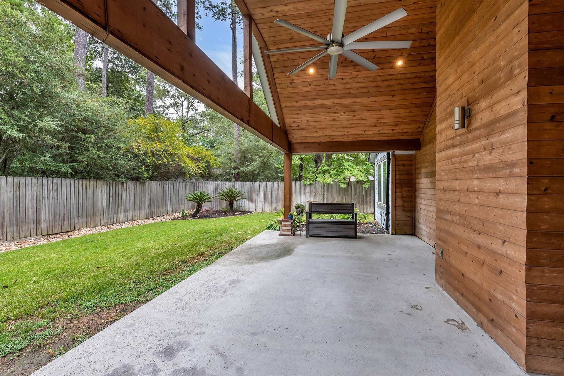 54 Sky Terrace Place, The Woodlands, TX 77381 Spacious covered patio with wooden paneling and ceiling fan, overlooking a lush, fenced backyard perfect for relaxation and outdoor gatherings.