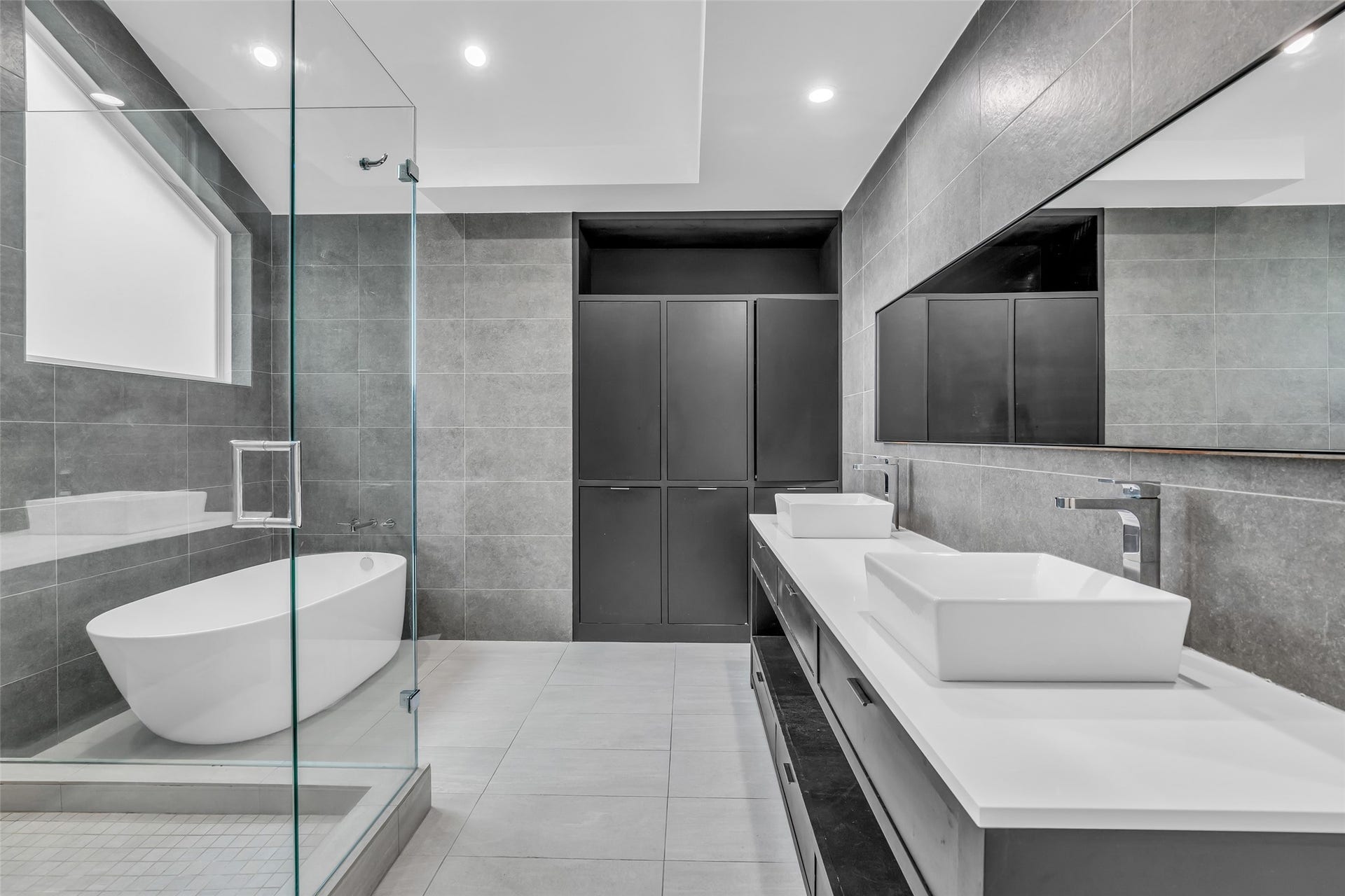 54 Sky Terrace Place, The Woodlands, TX 77381 Luxurious modern bathroom featuring a sleek freestanding tub, dual sinks, and a spacious glass-enclosed shower, all accented by elegant gray tile and ample storage.