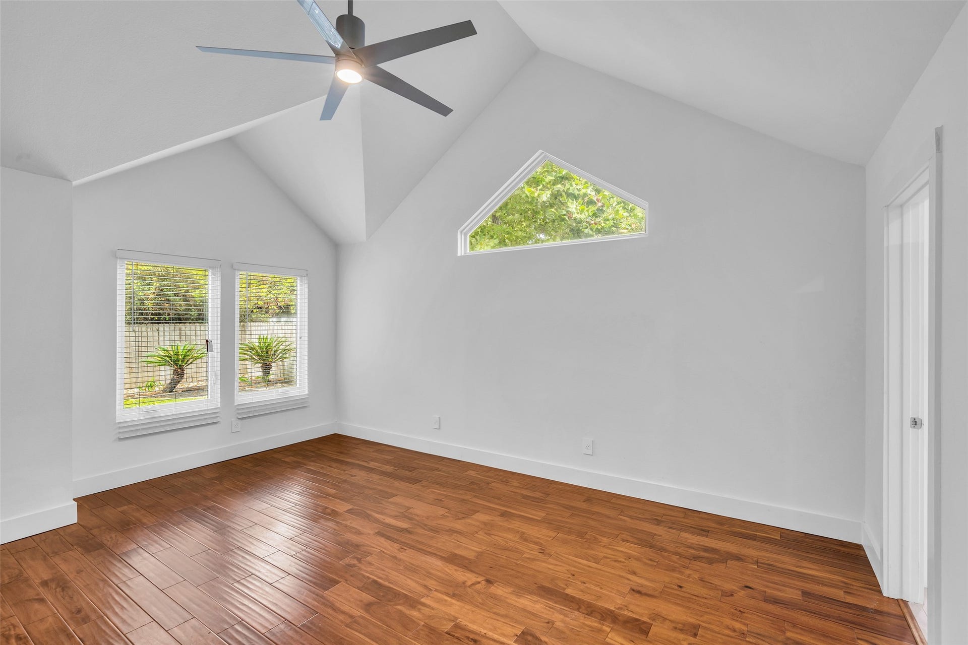 54 Sky Terrace Place, The Woodlands, TX 77381 Spacious first-floor primary bedroom featuring vaulted ceilings, rich hardwood floors, and large windows that fill the room with natural light while offering peaceful views of the backyard.