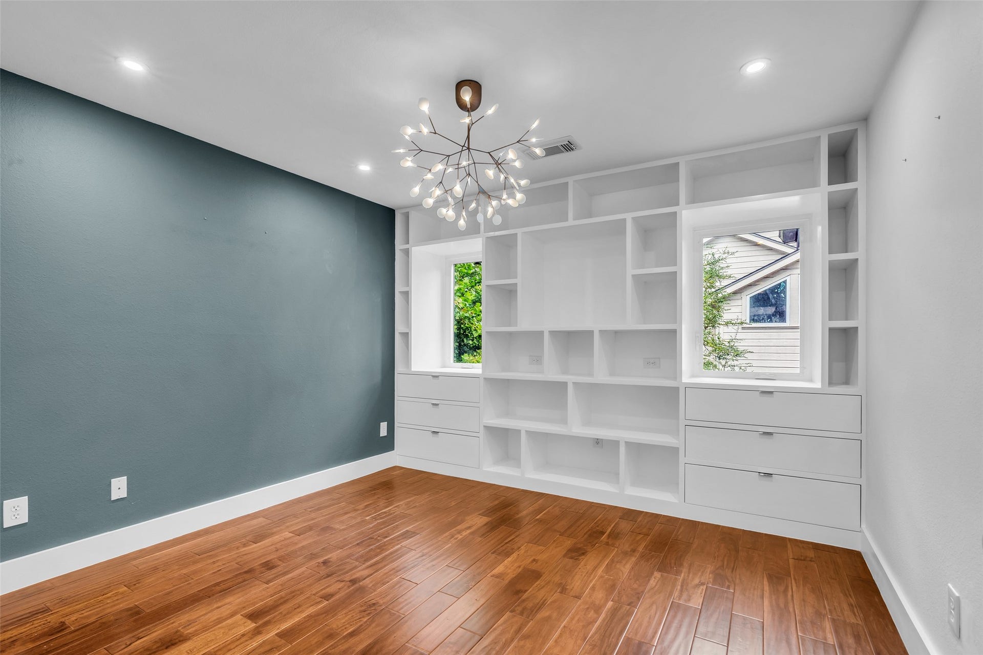 54 Sky Terrace Place, The Woodlands, TX 77381 Elegant 2nd room with rich hardwood floors, a striking modern chandelier, and built-in shelving offering ample storage. A large window provides natural light and a calming view.