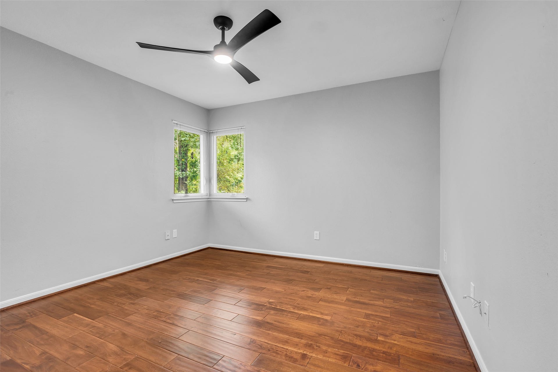 54 Sky Terrace Place, The Woodlands, TX 77381 Spacious 3rd bedroom with warm hardwood floors, neutral walls, and a modern ceiling fan, complemented by natural light from the corner windows.