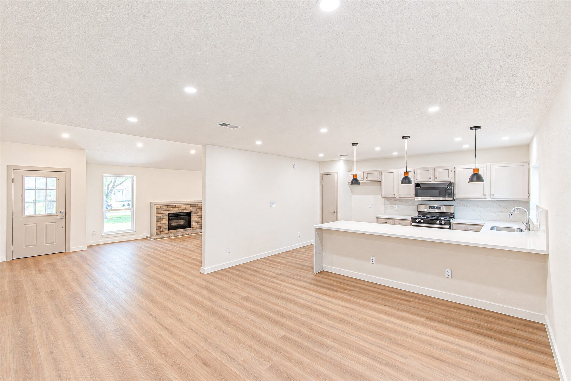18015 Brooknoll Drive, Houston, TX 77084 Spacious open-concept living area with modern kitchen, featuring sleek countertops, pendant lighting, and a cozy fireplace, complemented by beautiful wood flooring.