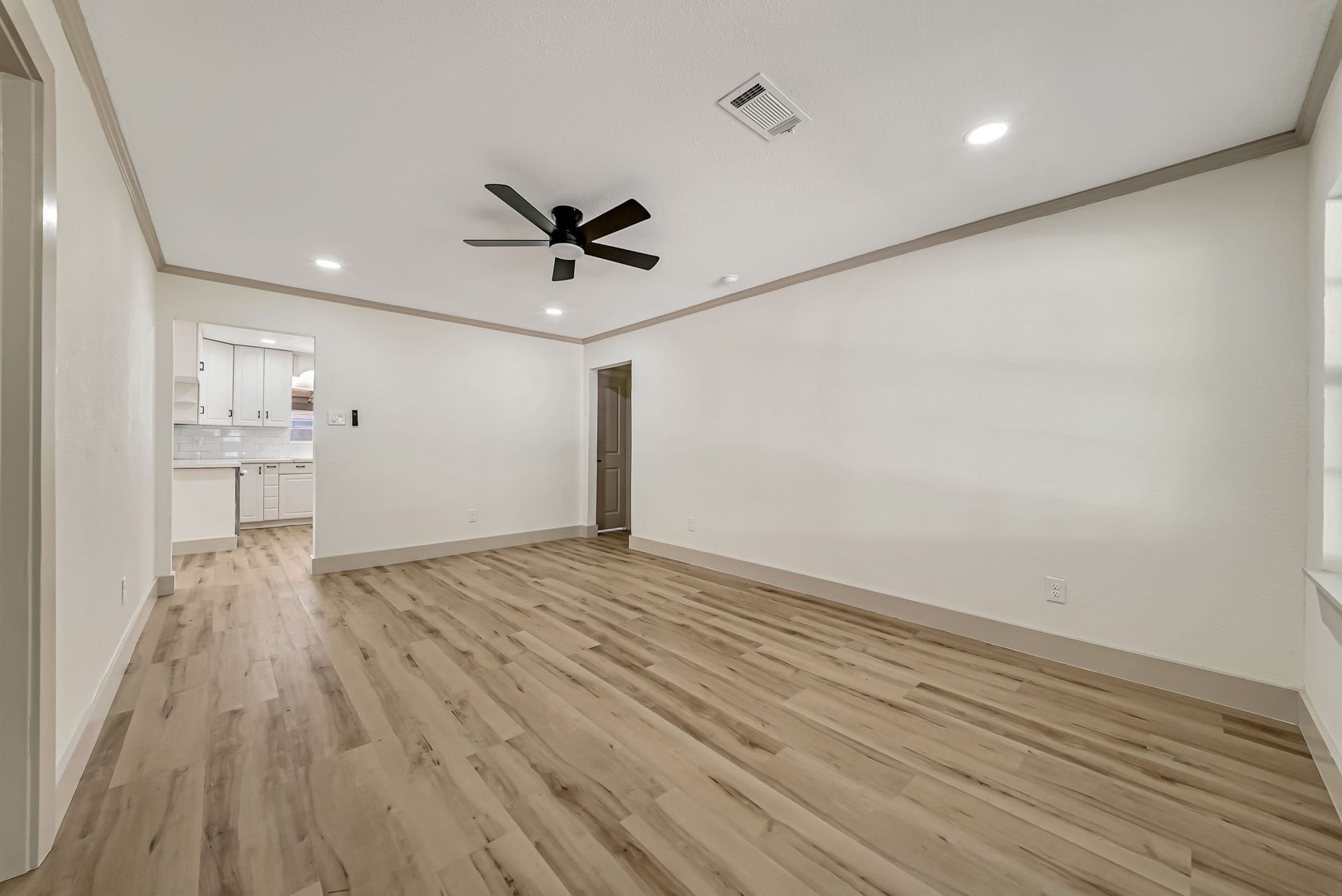 6638 Thornwall Street, Houston, TX 77092 Spacious living room with elegant wood like flooring, modern ceiling fan, and recessed lighting, seamlessly connecting to a bright kitchen.