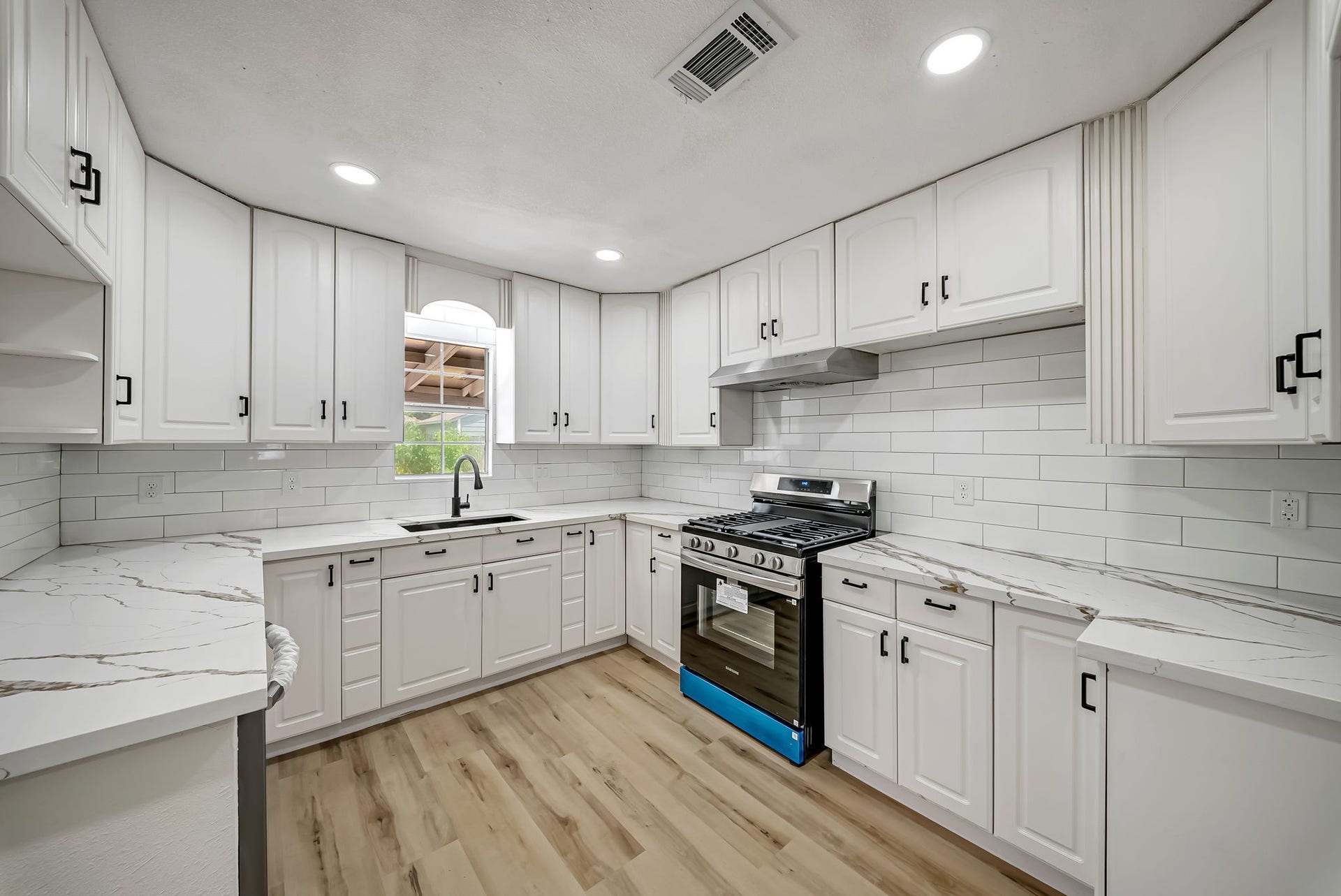 6638 Thornwall Street, Houston, TX 77092 Elegant kitchen with sleek white cabinetry, modern stainless steel appliances, and stylish quartz countertops, all complemented by a chic subway tile backsplash and warm LVP flooring.