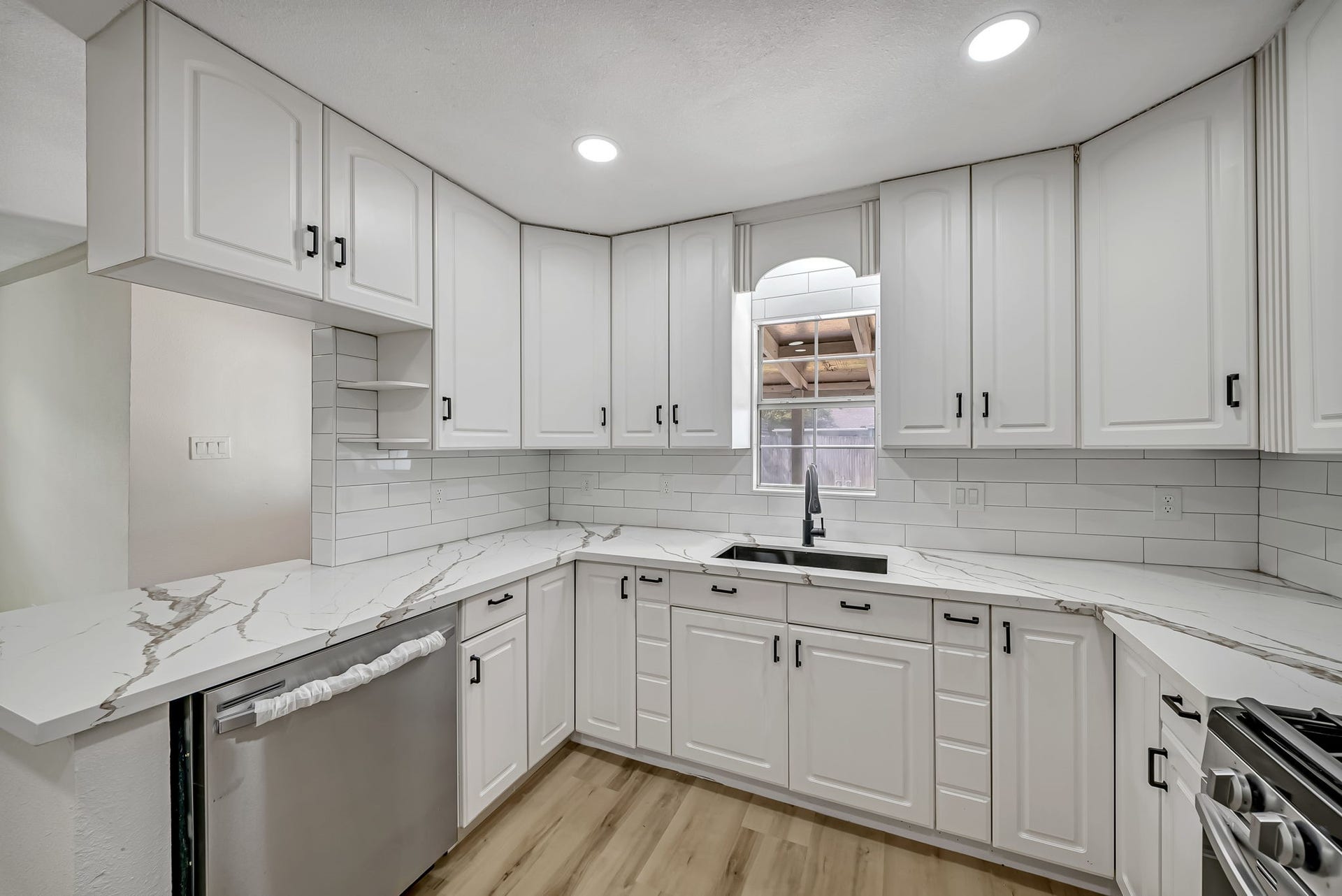 6638 Thornwall Street, Houston, TX 77092 Elegant kitchen featuring pristine white cabinetry, sleek quartz countertops, and modern stainless steel appliances, complemented by a large window that invites natural light.