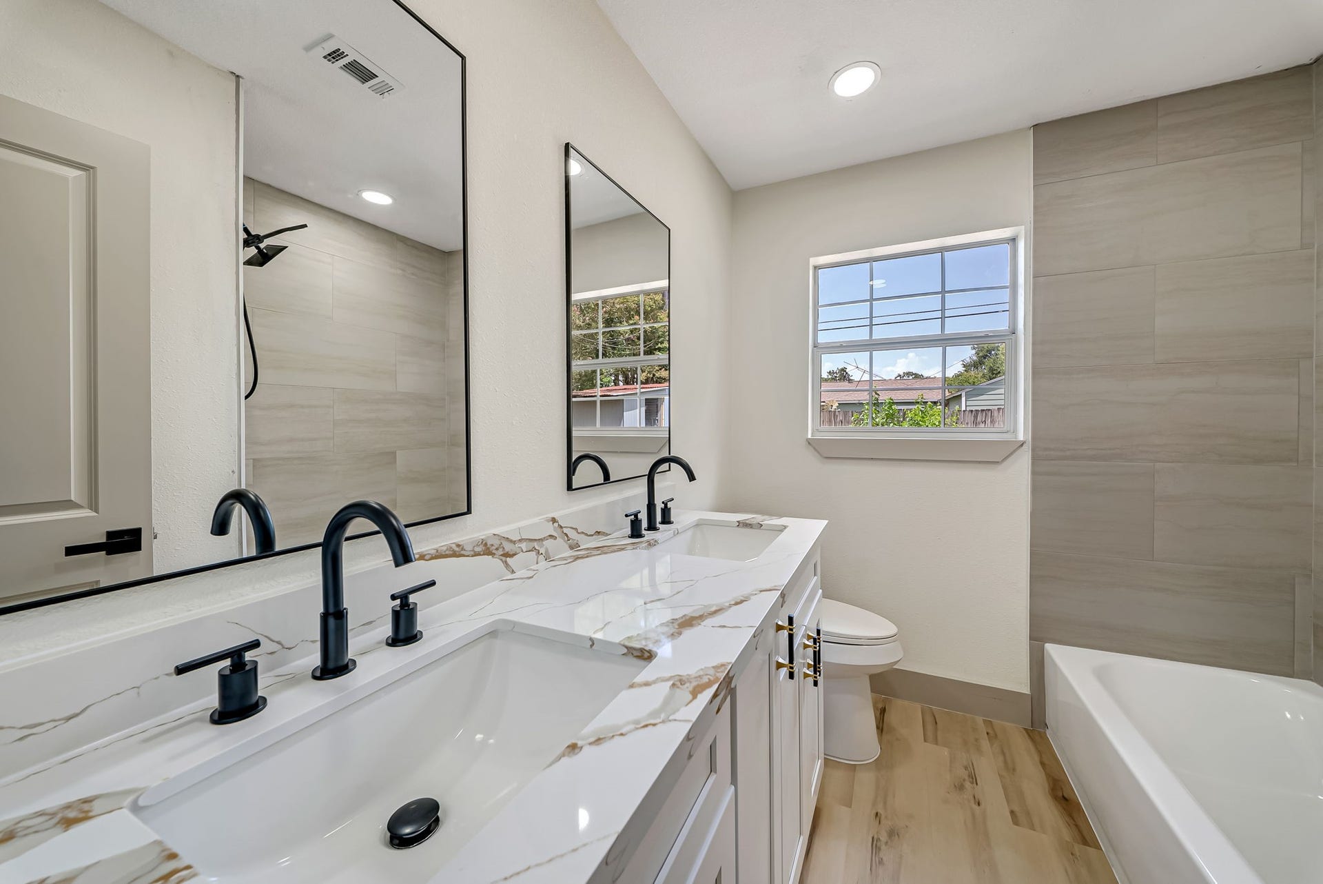6638 Thornwall Street, Houston, TX 77092 Elegant bathroom featuring a dual-sink vanity with sleek black fixtures, large modern mirrors, and a stylish mix of marble and wood accents.