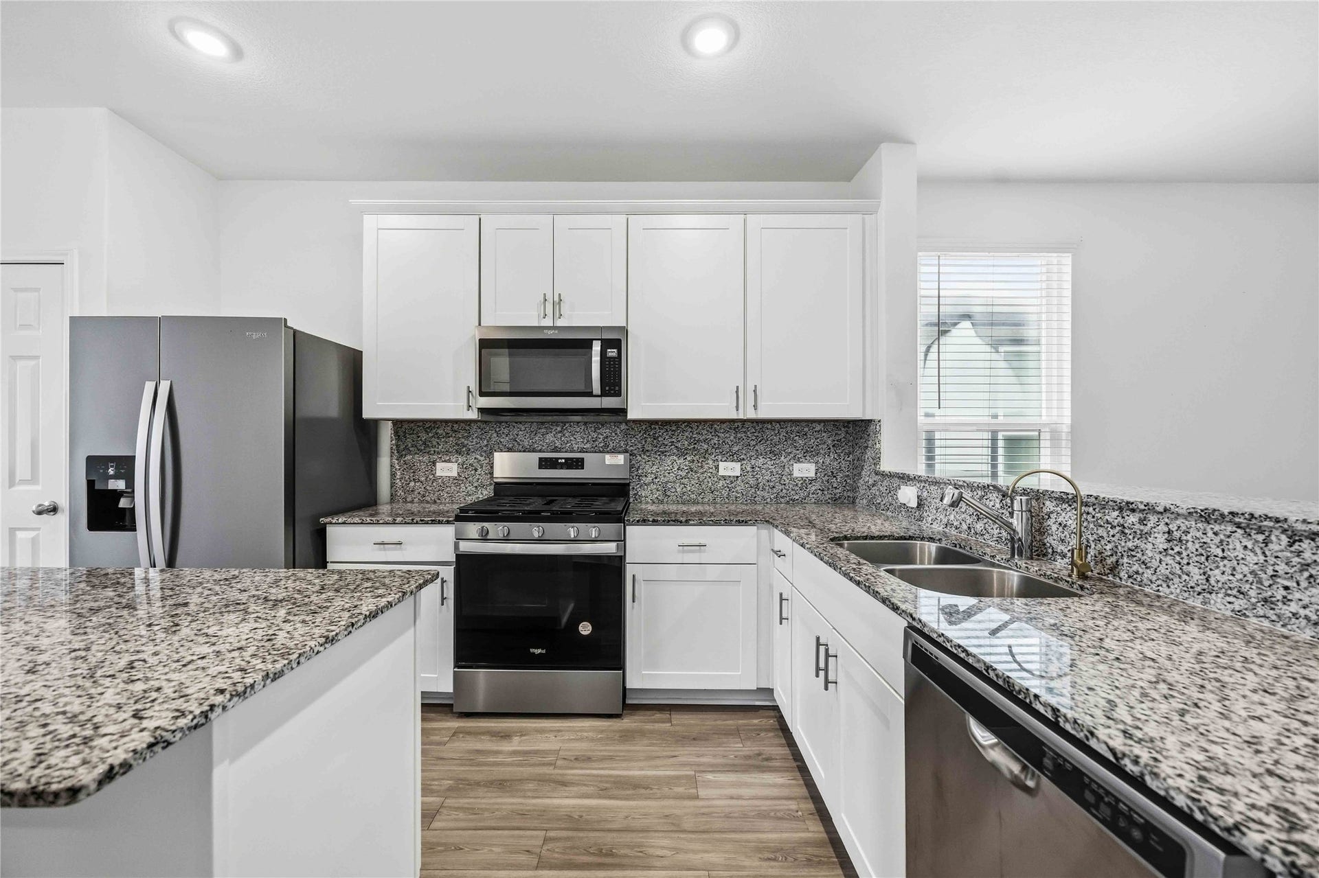 Stainless steel appliances complement granite countertops and backsplash.
