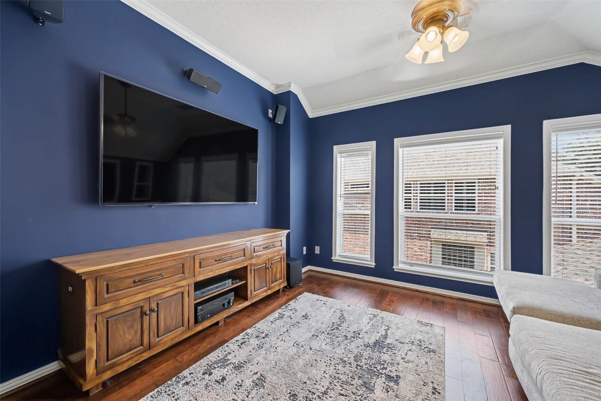 2907 Winding Shore Lane, Katy, TX 77450 A cozy media room features rich blue walls, a large mounted TV, and elegant wood flooring, complemented by ample natural light from multiple windows.