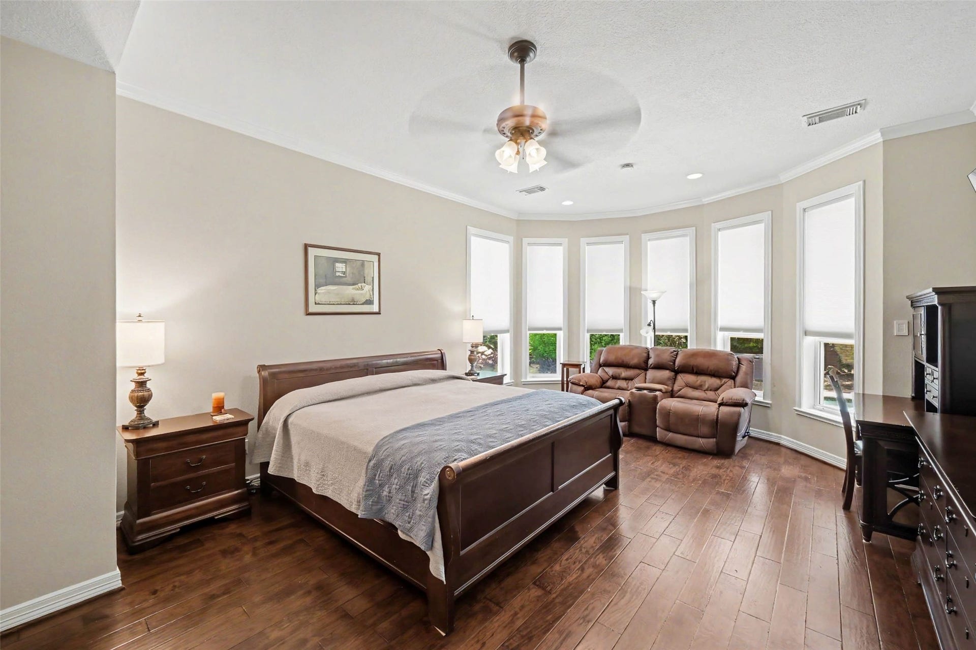 2907 Winding Shore Lane, Katy, TX 77450 Spacious and bright bedroom featuring elegant hardwood floors, a cozy seating area by large bay windows, and a ceiling fan for added comfort.