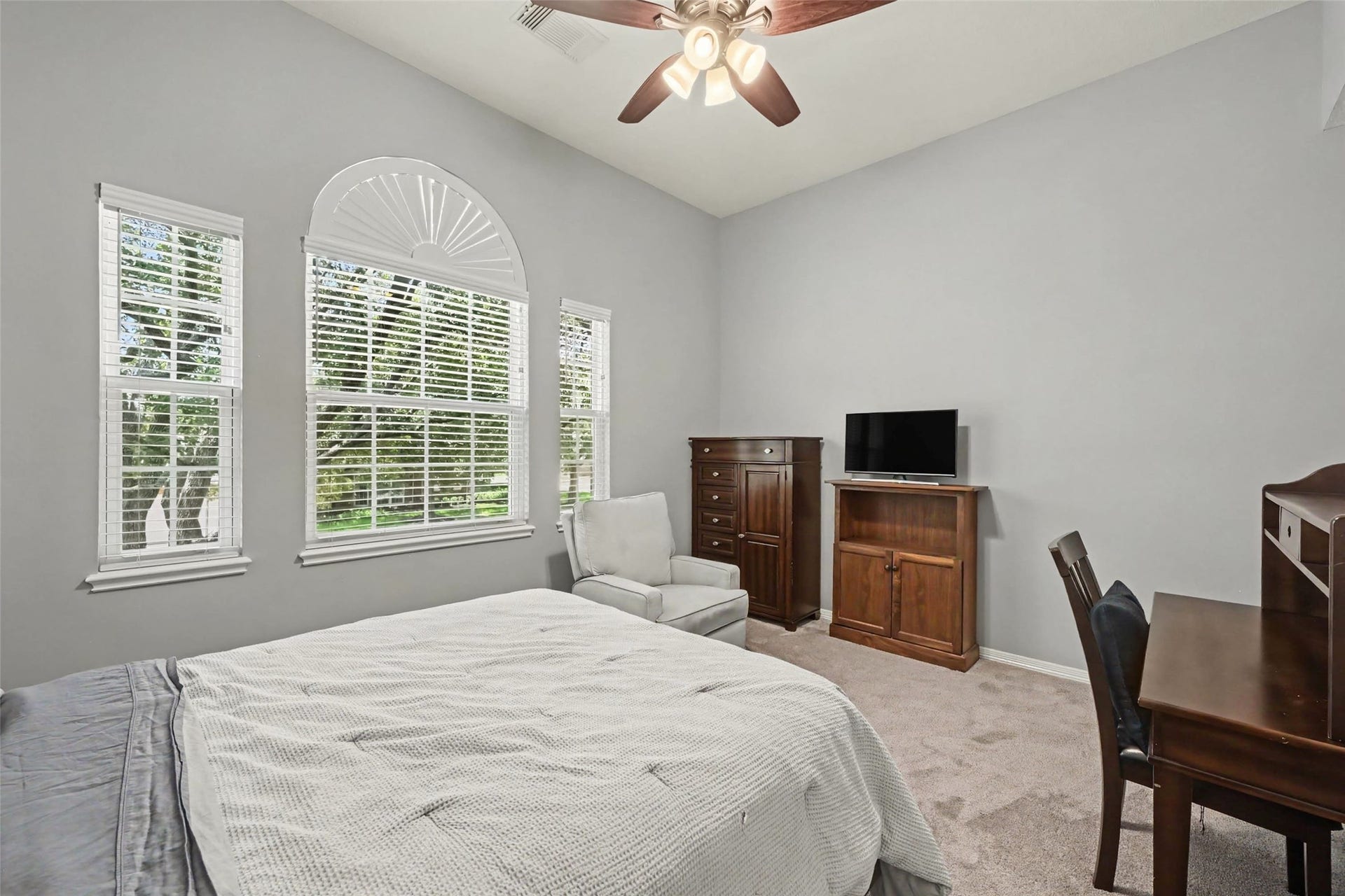 2907 Winding Shore Lane, Katy, TX 77450 Spacious bedroom with large arched windows, allowing natural light to enhance the serene ambiance. It features a cozy sitting area and a ceiling fan for added comfort.