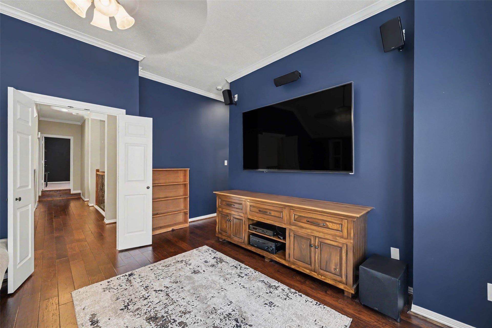 2907 Winding Shore Lane, Katy, TX 77450 Stylish media room with rich blue walls, hardwood floors, and built-in surround sound, featuring a large flat-screen TV and elegant wooden cabinetry.
