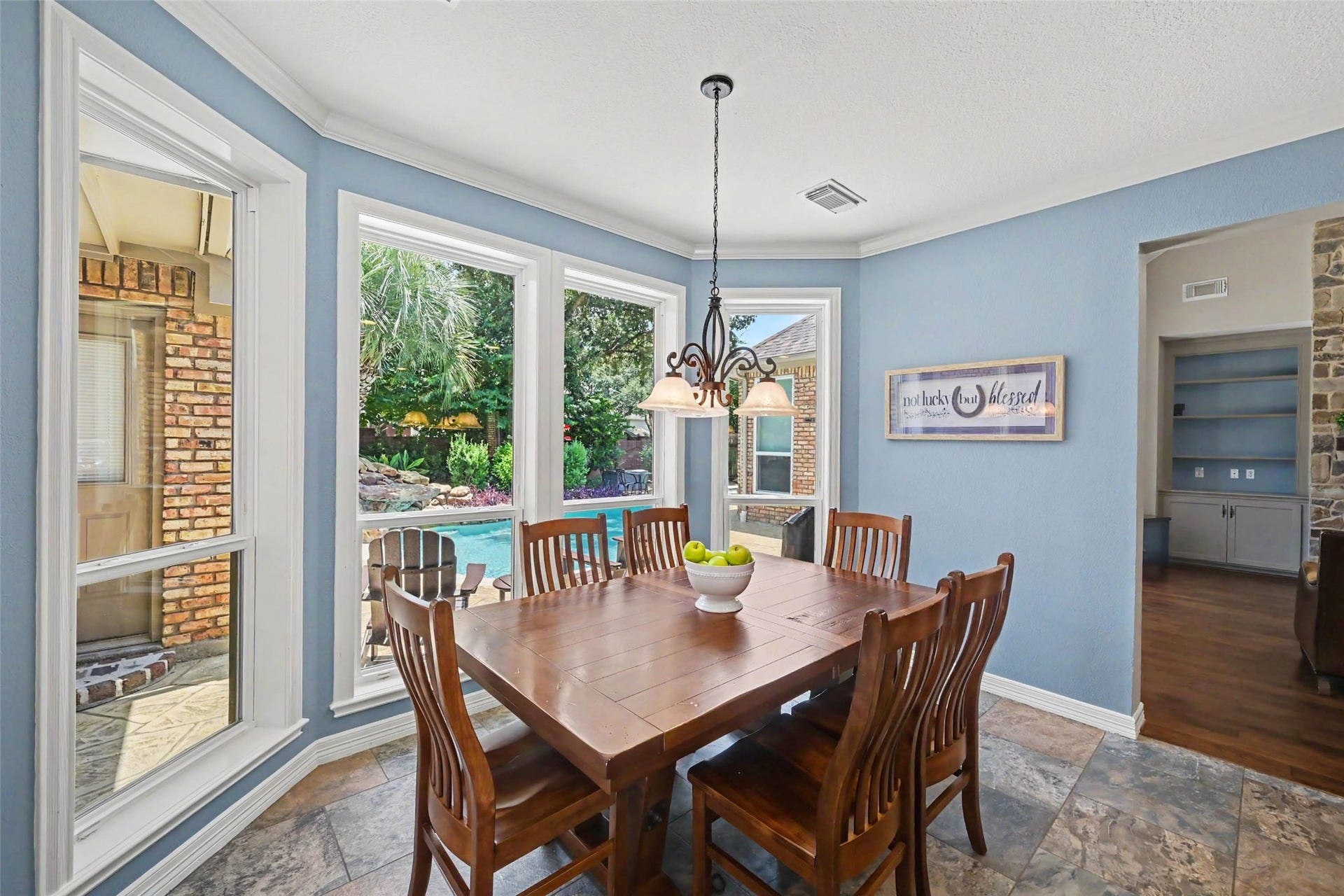 2907 Winding Shore Lane, Katy, TX 77450 Bright dining area with large windows offering a stunning view of the backyard pool and lush greenery, complemented by elegant tile flooring and a charming chandelier.