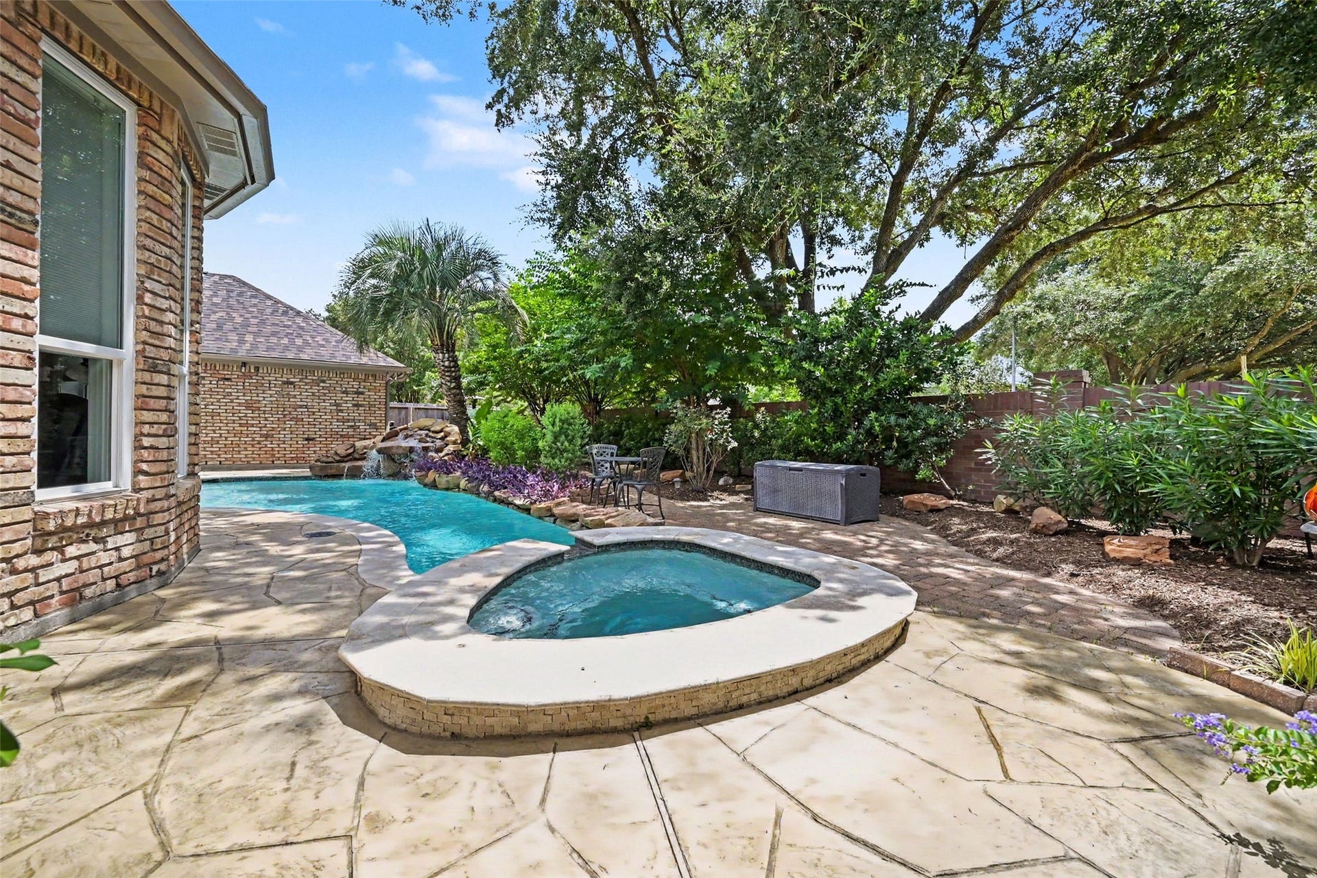 2907 Winding Shore Lane, Katy, TX 77450 Charming backyard oasis featuring a sparkling pool and spa surrounded by lush greenery and mature trees, perfect for relaxation and entertaining.