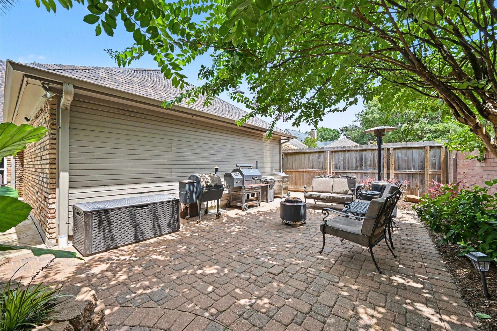 2907 Winding Shore Lane, Katy, TX 77450 Charming backyard patio with brick pavers, cozy seating, and a barbecue area, shaded by lush treesperfect for outdoor entertaining.