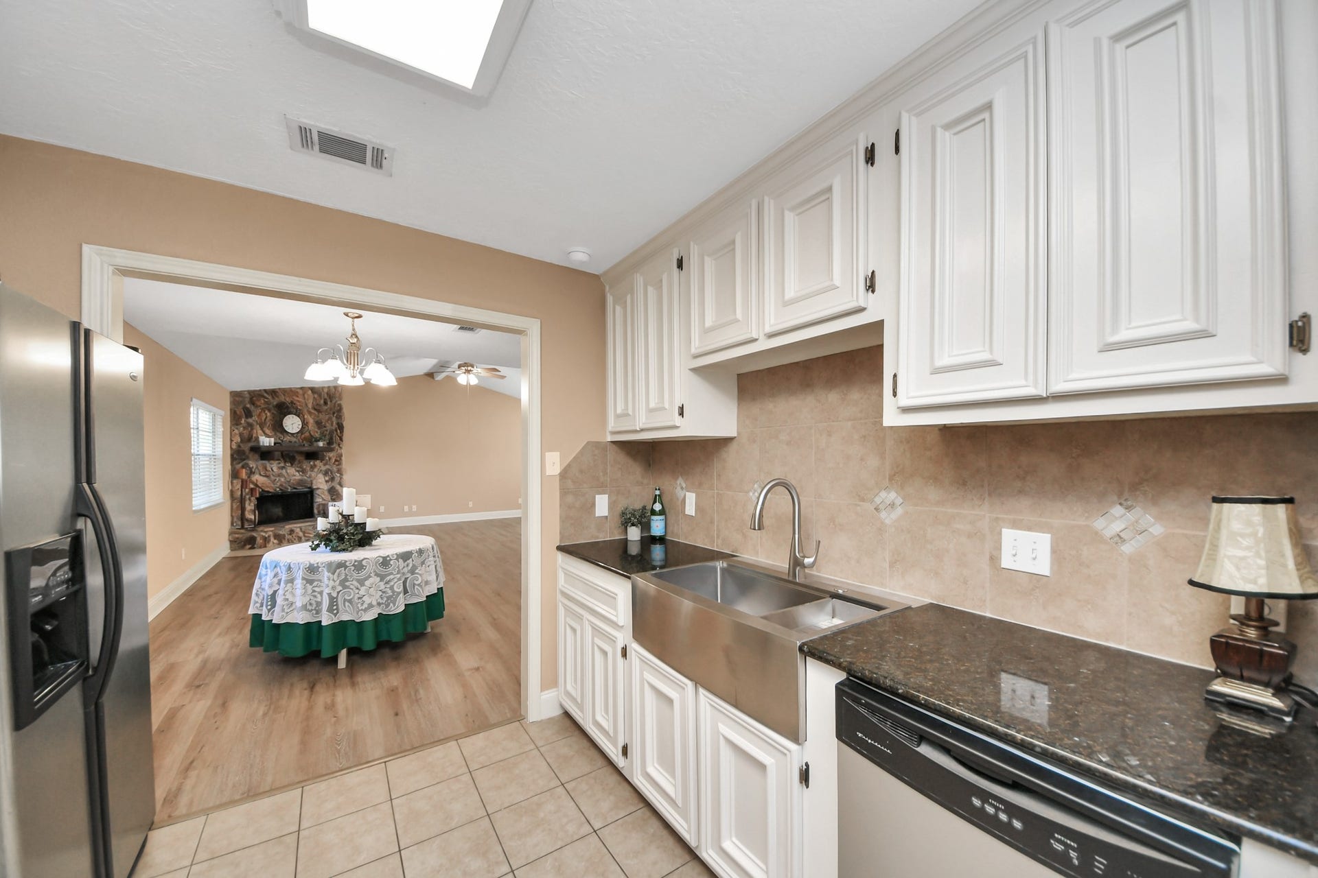 935 Grand Junction Drive, Katy, TX 77450 From cooking dinner to hosting memorable gatherings, this kitchens connection to the adjoining dining and living areas makes entertaining convenient. The galley-style layout features white cabinetry, dark countertops, stainless steel appliances, and a distinctive apron-front sink. Just beyond the kitchen, the dining area flows into a spacious living room anchored by a beautiful floor-to-ceiling stone fireplace.