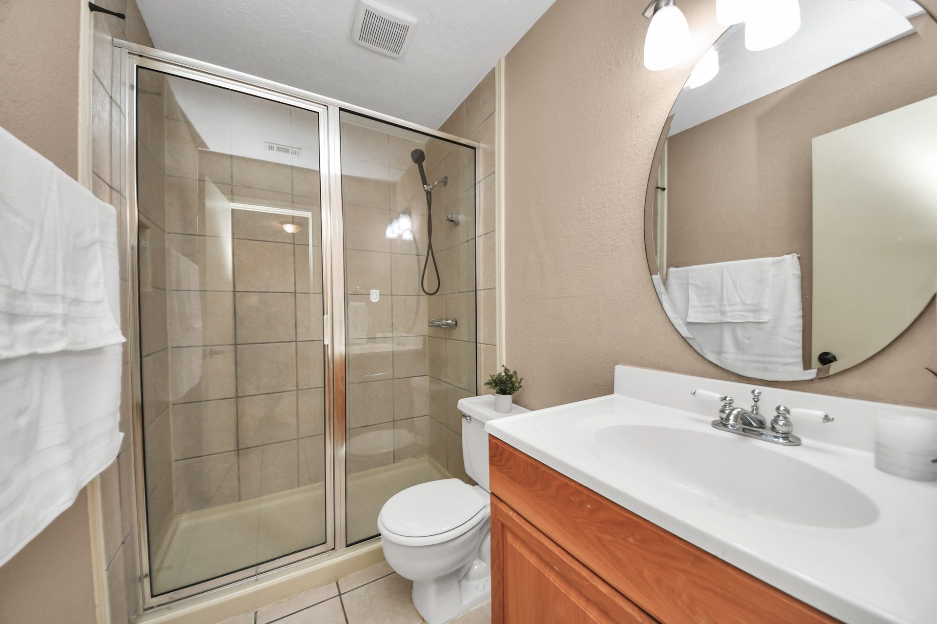 935 Grand Junction Drive, Katy, TX 77450 Perfectly positioned between the two first-level secondary bedrooms, this full bathroom offers easy access and everyday functionality. Featuring a spacious glass-enclosed shower with tile surround, a handheld showerhead, an oversized vanity countertop, and a stylish round mirror, this thoughtfully arranged space provides everything needed for a refreshing start or relaxing end to the day
