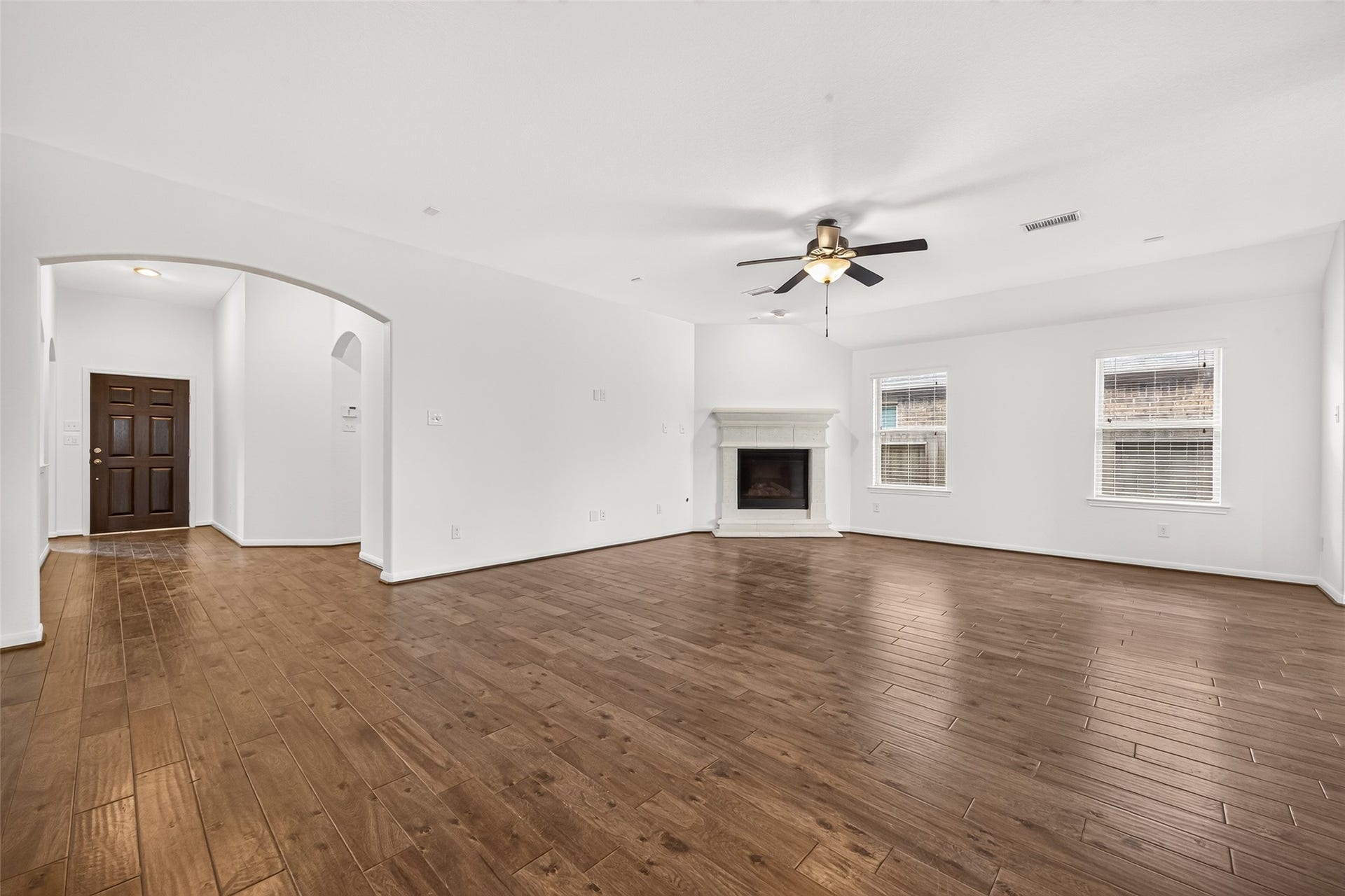 Light and bright living room with wood look floors, ceiling fan, and gas fireplace.