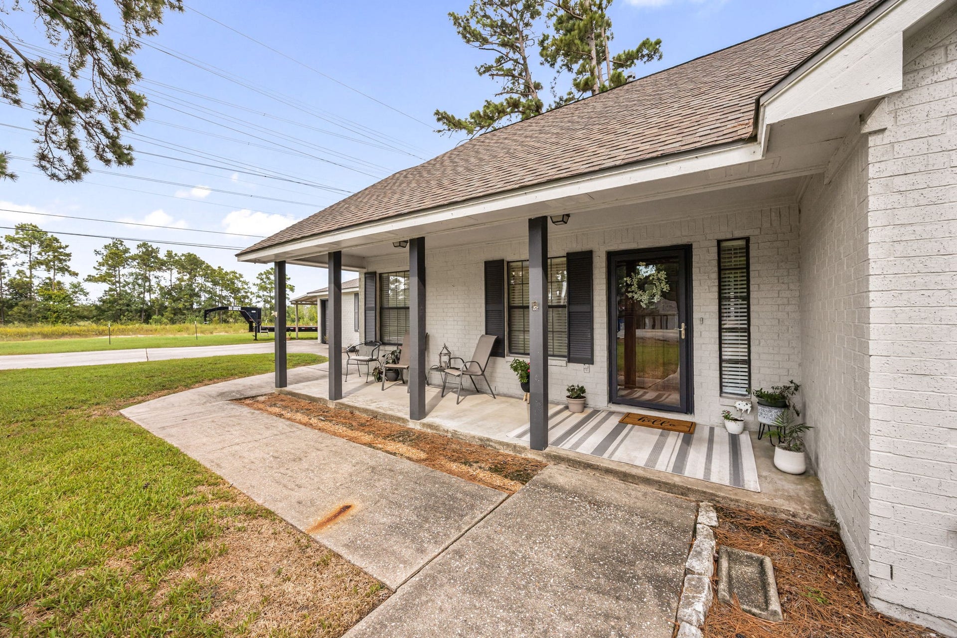 Covered front porch creates an inviting entrance framed by the homes mature, tree-filled setting.
