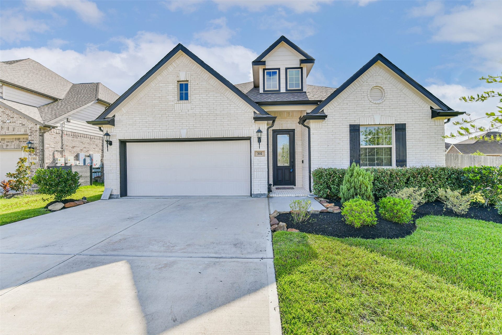 702 Campbell Drive, League City, TX 77573 Charming white brick home with black accents, featuring a spacious two-car garage and well-maintained landscaping.