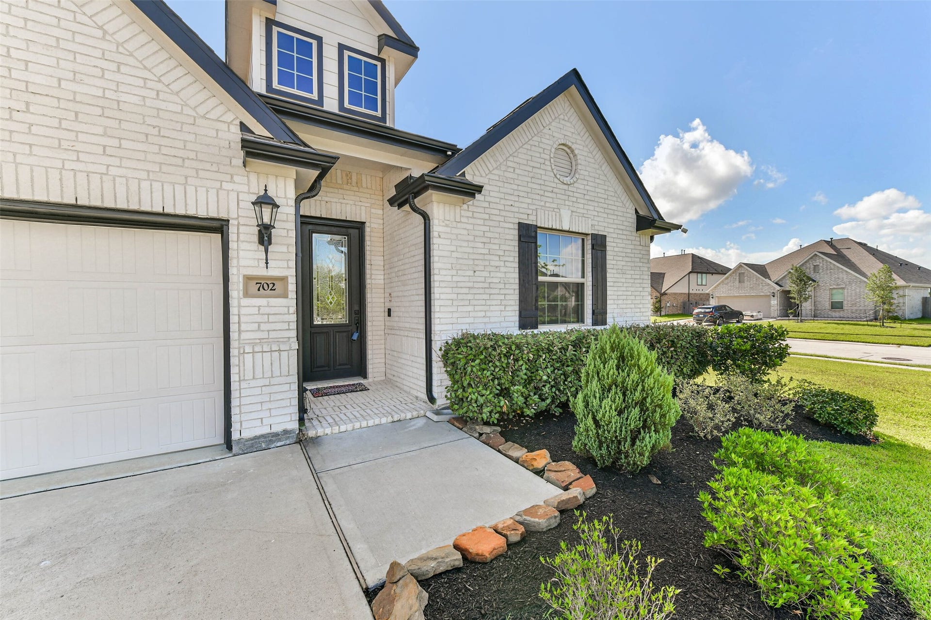 702 Campbell Drive, League City, TX 77573 Charming brick home with a welcoming entrance, beautifully manicured landscaping, and a modern exterior featuring a stylish black door and window shutters.