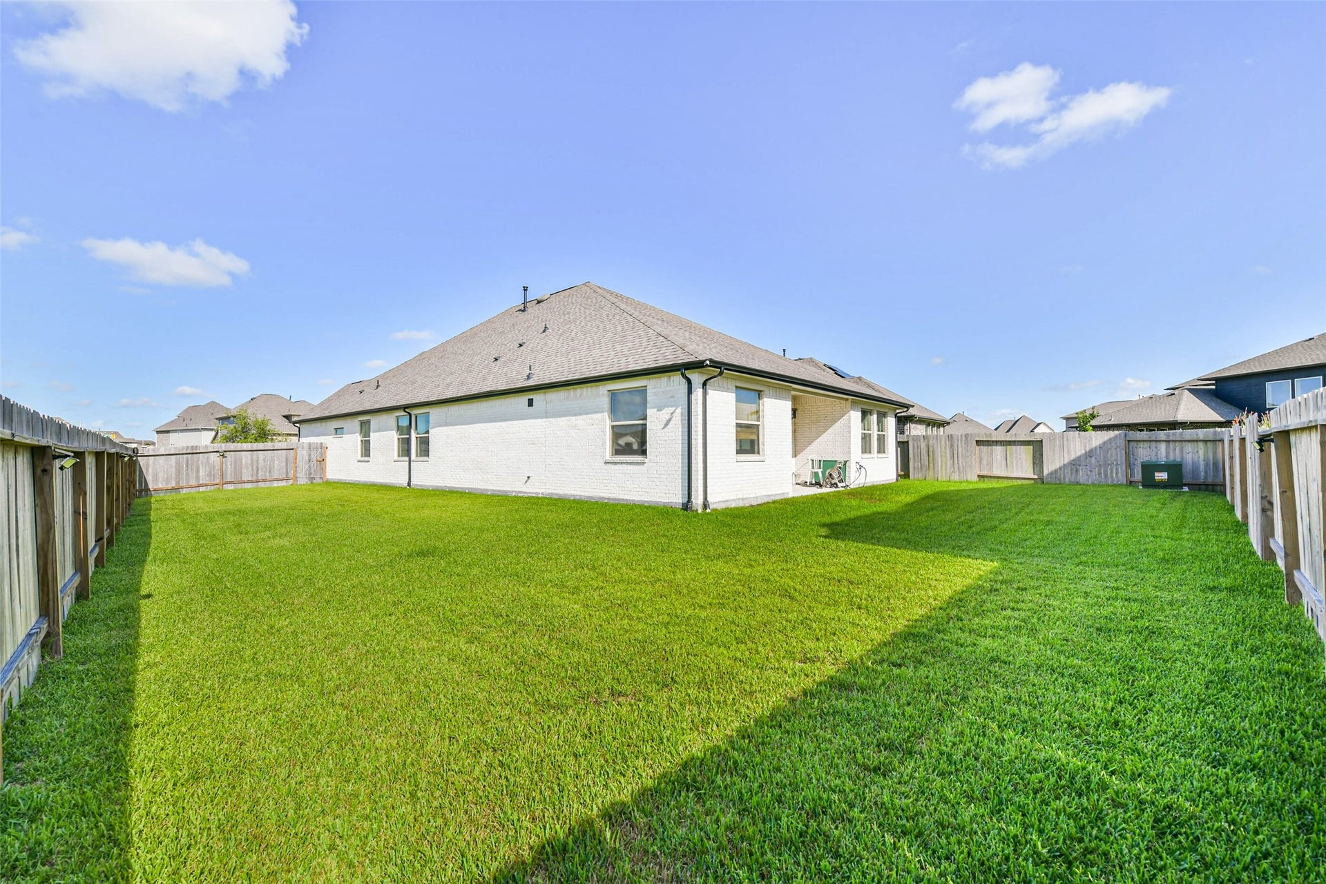 702 Campbell Drive, League City, TX 77573 Spacious backyard with lush green lawn, perfect for outdoor activities, surrounded by a privacy fence and adjacent to a charming brick home.
