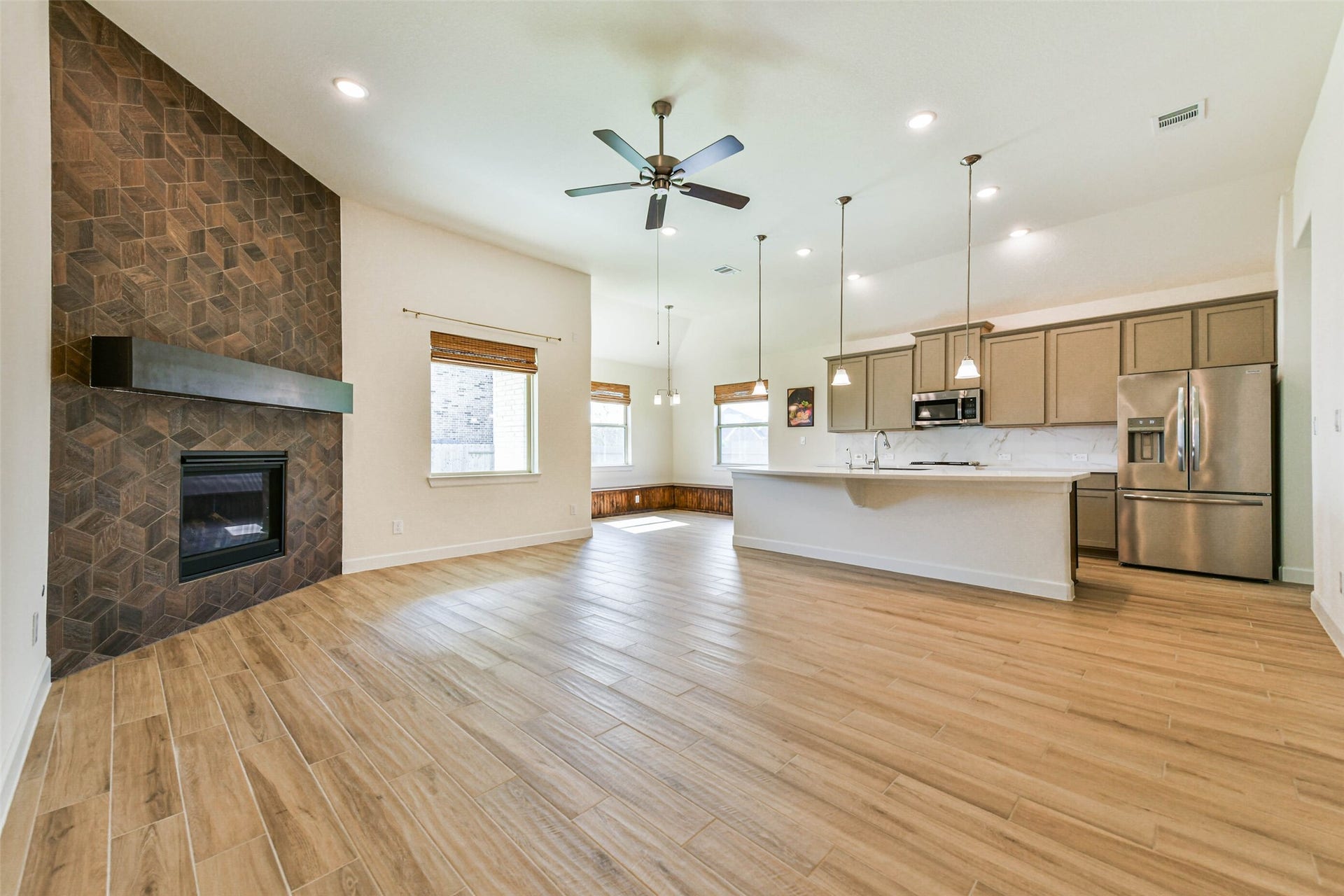 702 Campbell Drive, League City, TX 77573 Spacious open-concept living area featuring a modern kitchen with stainless steel appliances, a cozy living room with a stylish tiled fireplace, and elegant wood flooring throughout.