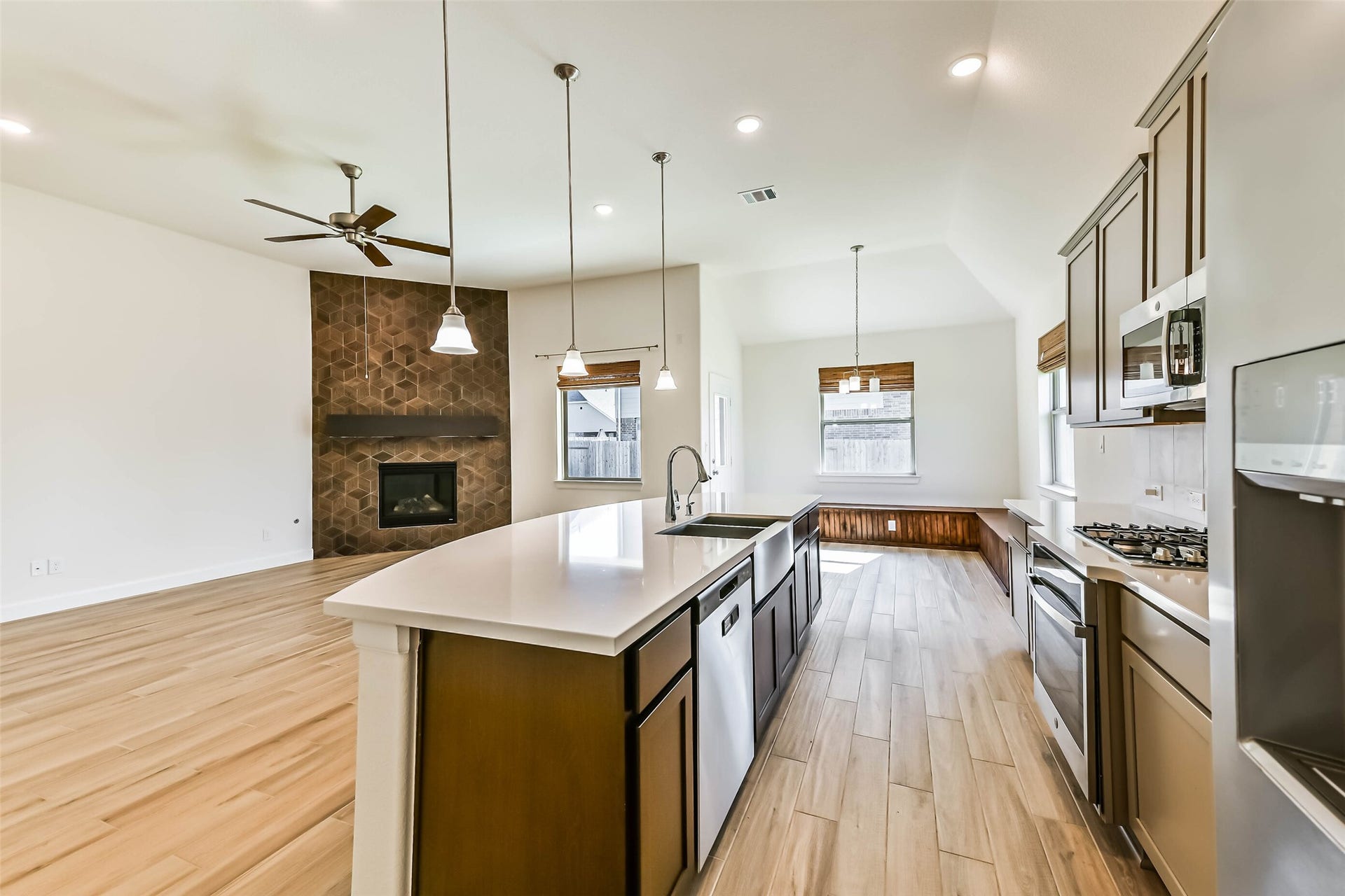 702 Campbell Drive, League City, TX 77573 Bright and open kitchen and living area featuring a modern island with dual sinks, stylish cabinetry, and stainless steel appliances. A cozy fireplace with unique tile design enhances the spacious living room, while large windows bring in abundant natural light.