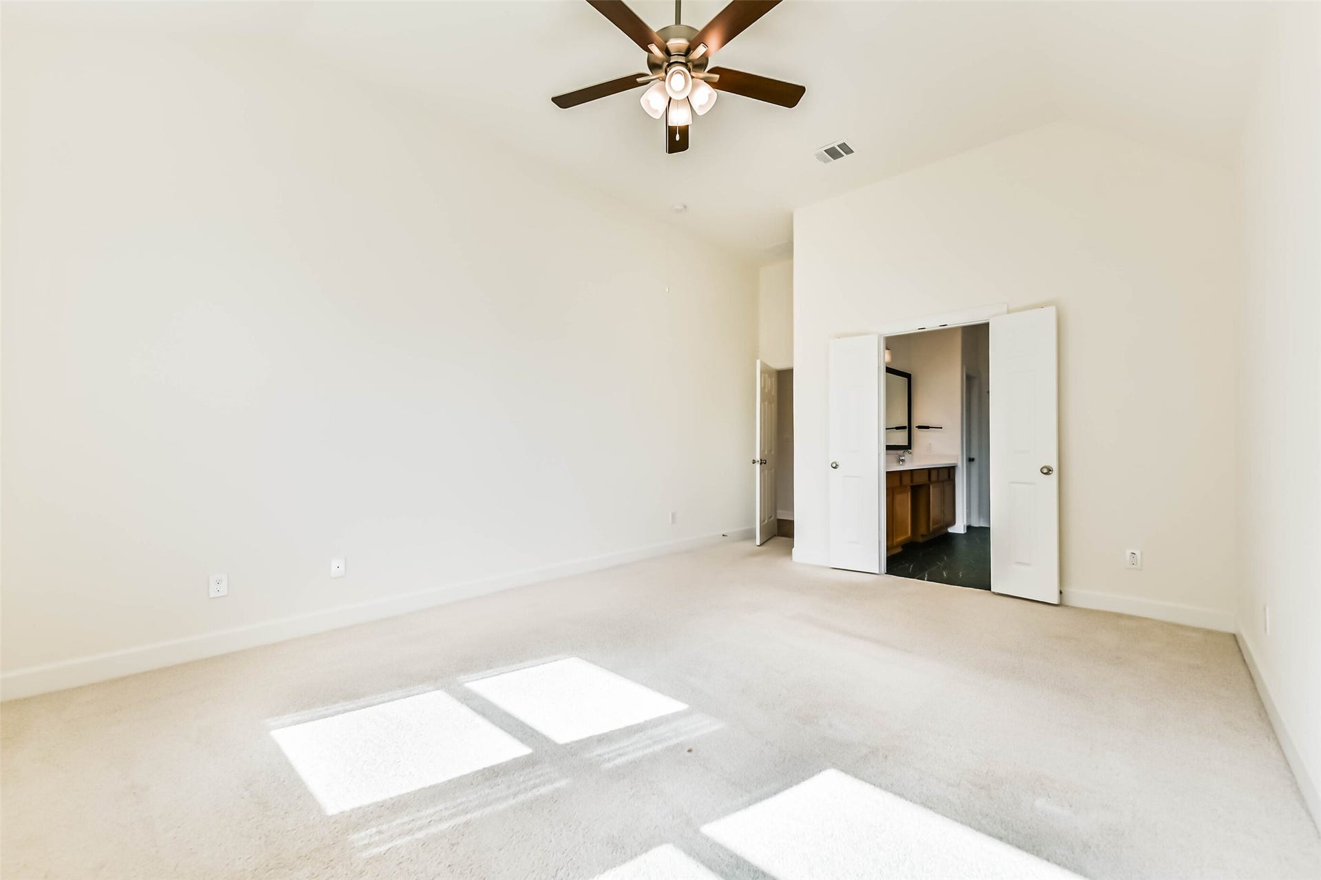 702 Campbell Drive, League City, TX 77573 Another view of the primary bedroom with high ceilings, abundant natural light, and a ceiling fan, leading to an ensuite bathroom through double doors.