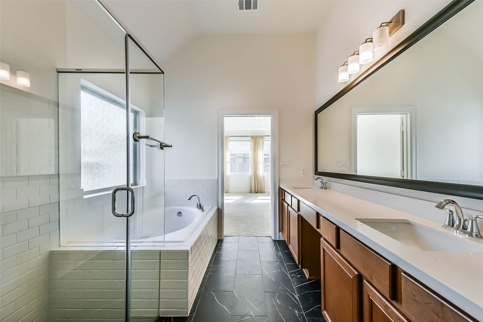 702 Campbell Drive, League City, TX 77573 Spacious primary bathroom featuring a luxurious glass-enclosed shower, a relaxing soaking tub, dual sinks with elegant fixtures, and sleek black tile flooring.