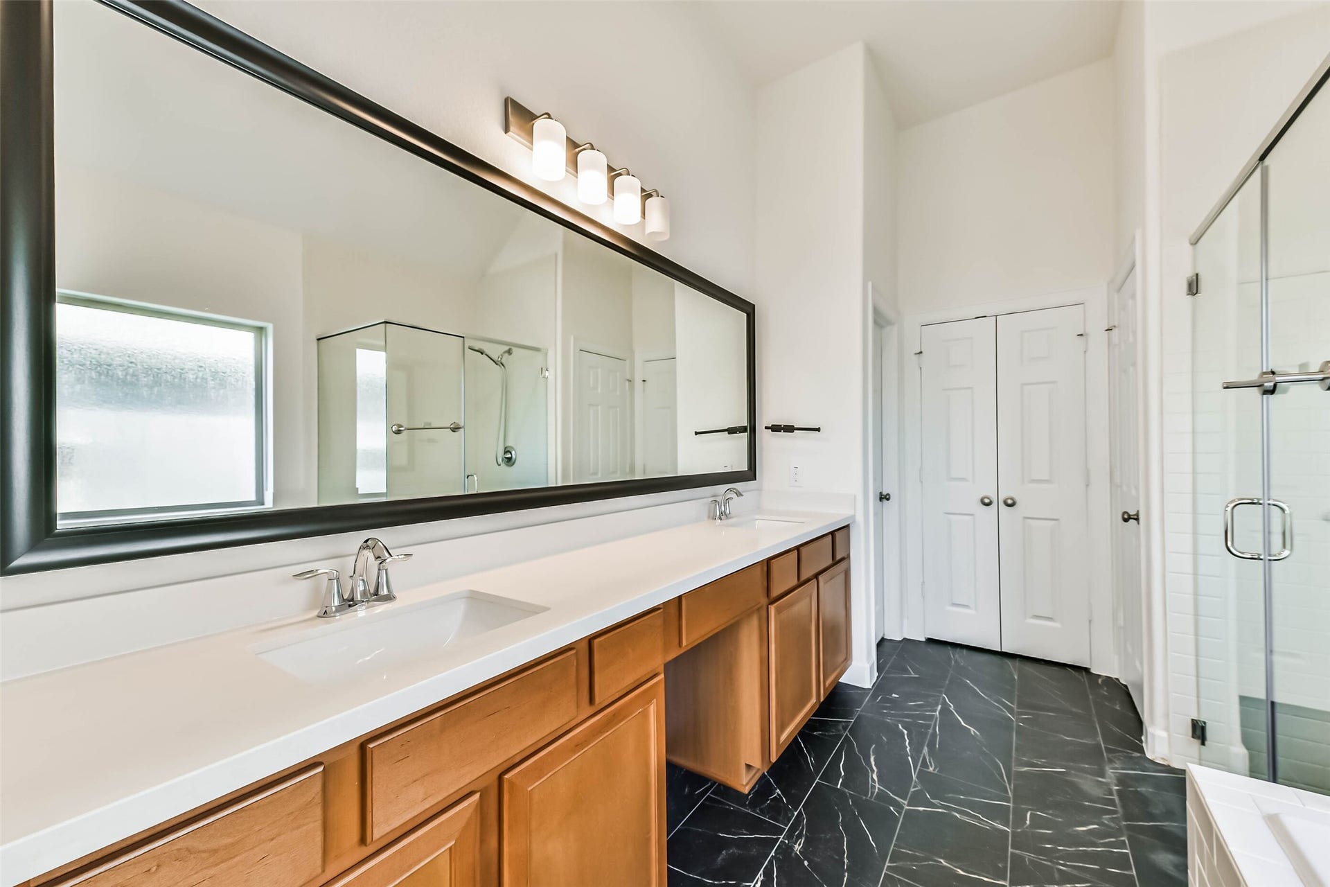 702 Campbell Drive, League City, TX 77573 Spacious primary bathroom featuring a double vanity with sleek countertops, a large mirror, elegant black-tiled flooring, and a glass-enclosed shower for a luxurious touch.