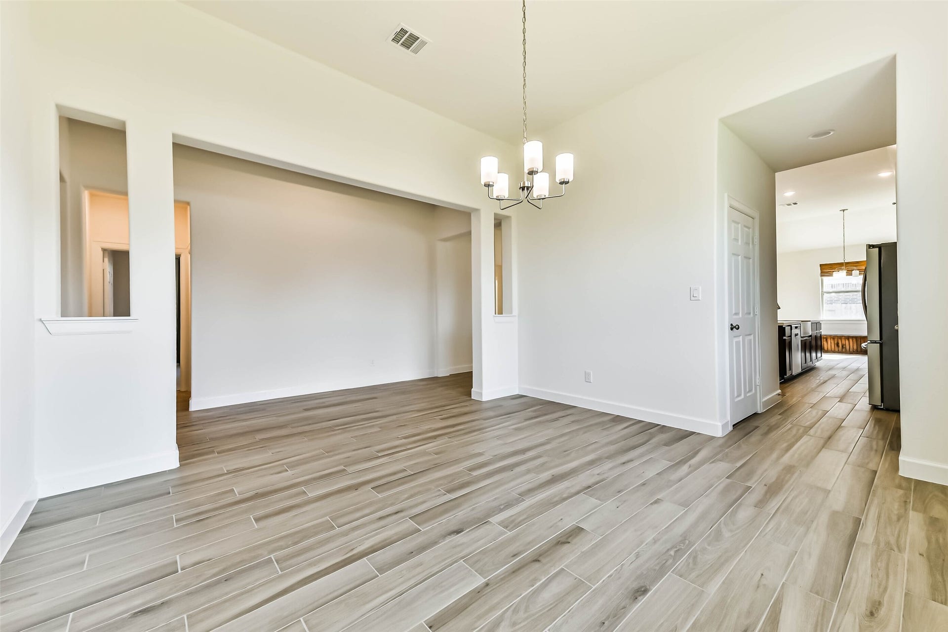 702 Campbell Drive, League City, TX 77573 Spacious dining area with elegant wood-look tile flooring, modern chandelier, and open access to the kitchen, creating a seamless flow for entertaining.